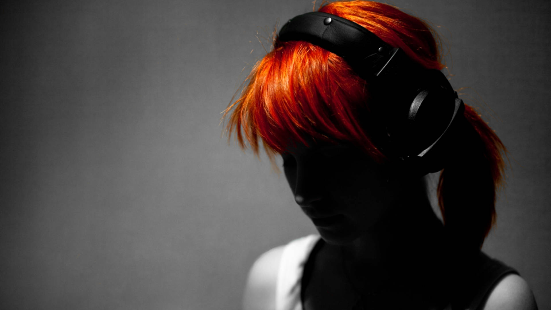 Hayley Williams 桌布 壁紙 — 一個擁有鮮豔紅髮的人戴著黑色耳機，在灰色背景前拍攝光線強烈、陰影分明的肖像照。