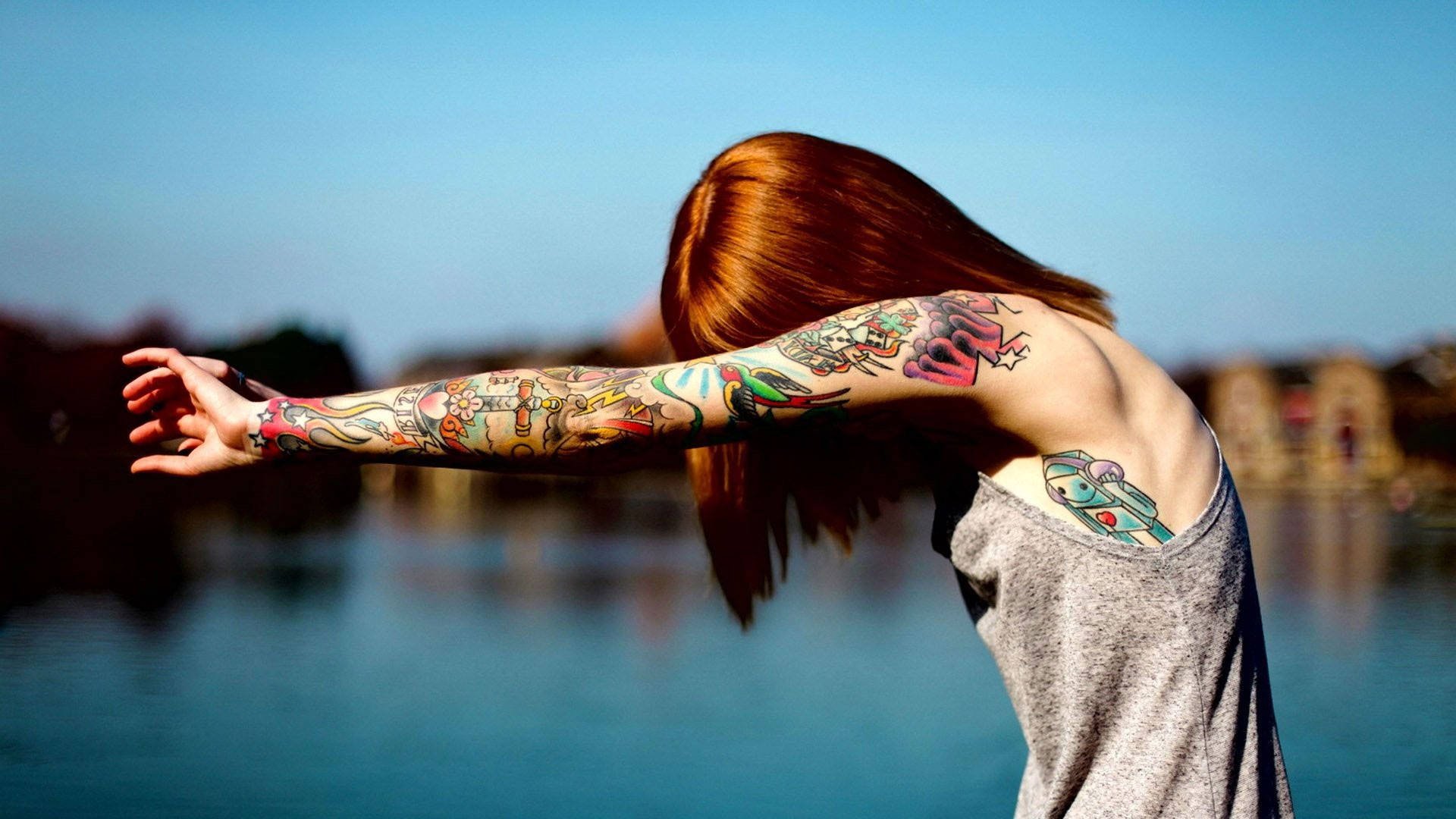 Tattoo 桌布 壁紙 — 一個擁有鮮豔紋身的人在晴朗的藍天下，在平靜的湖邊張開雙臂。