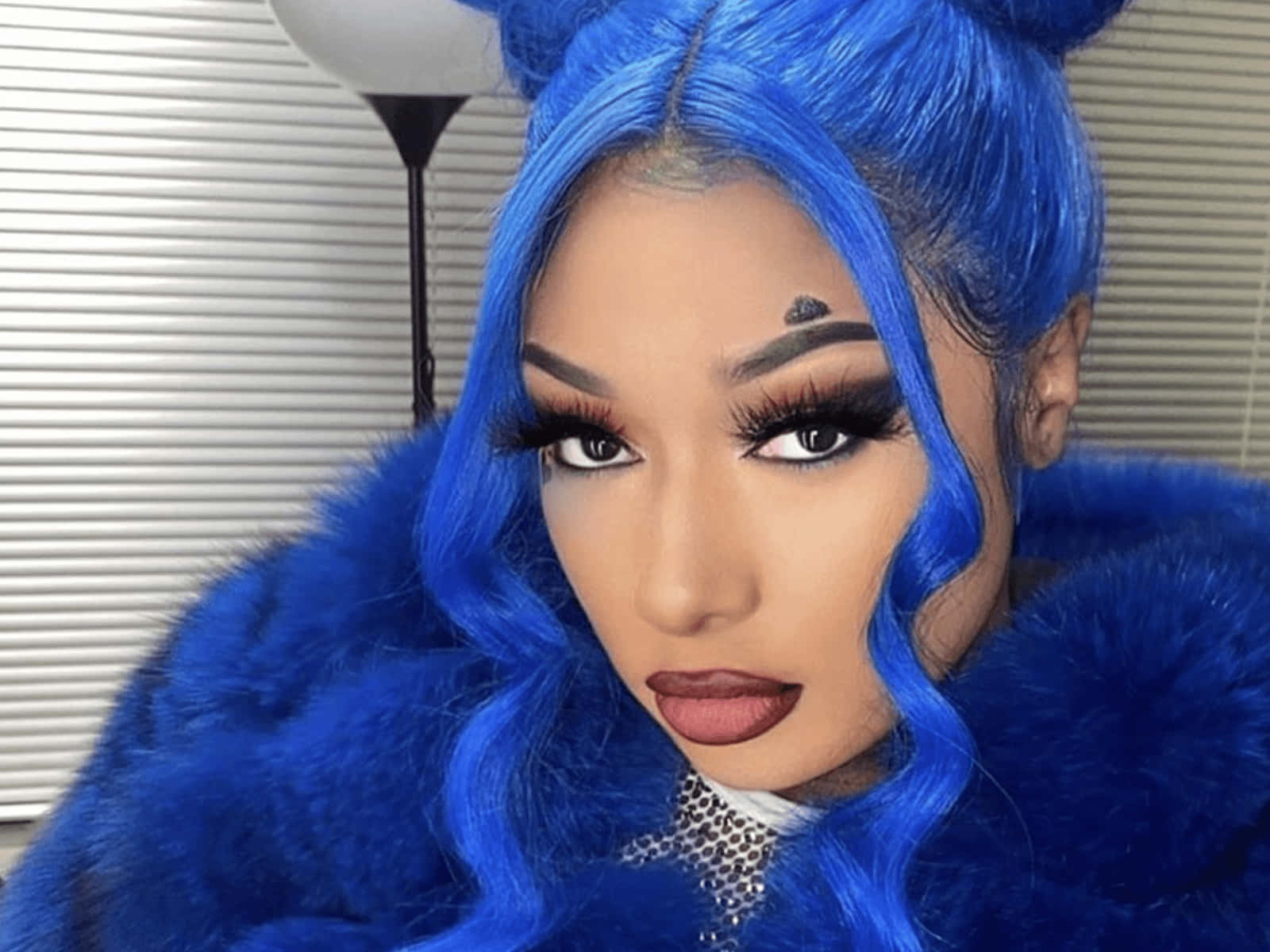 Megan Thee Stallion 桌布 壁紙 — 一個擁有鮮豔藍色頭髮和相配毛皮大衣的人，在百葉窗附近自信地擺姿勢。