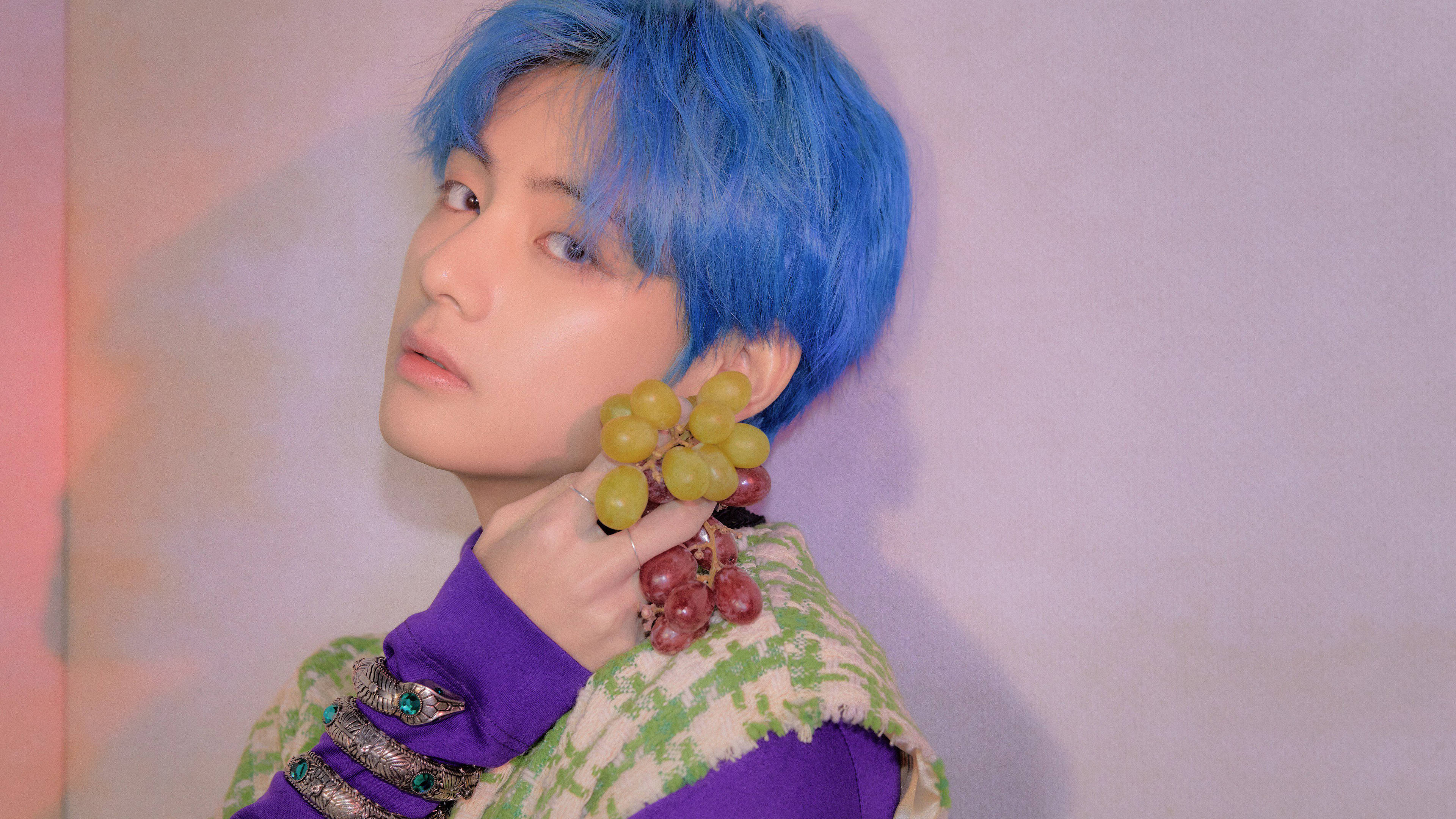 BTS 桌布 壁紙 — 一個擁有鮮豔藍色頭髮的人，手持一串綠色和紅色的葡萄，背景是柔和的粉紅色和薰衣草漸變牆。