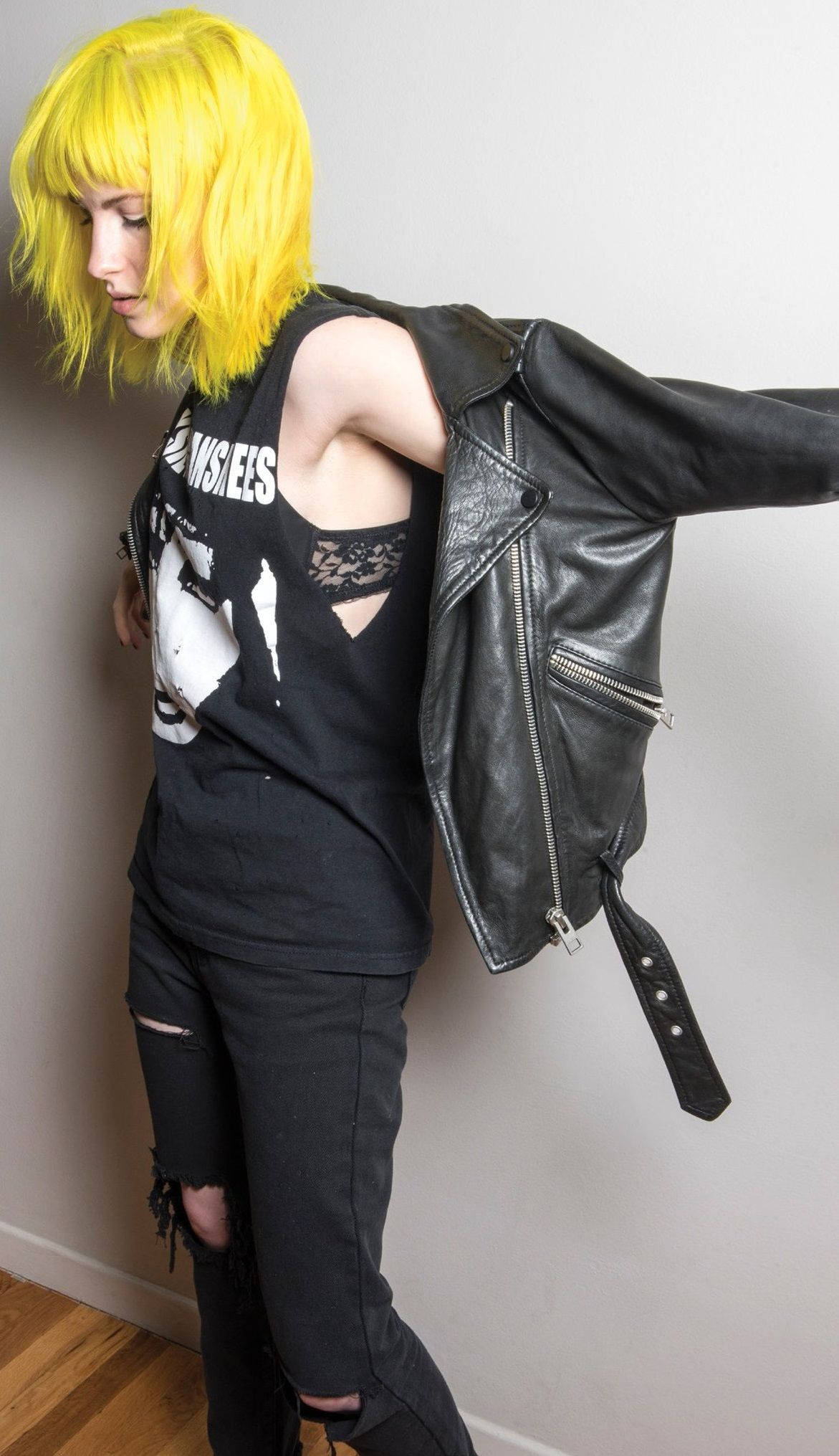 Hayley Williams 桌布 壁紙 — 一個擁有鮮豔黃色頭髮的人靠著牆，穿著黑色皮夾克，內搭圖案T恤和破洞牛仔褲。