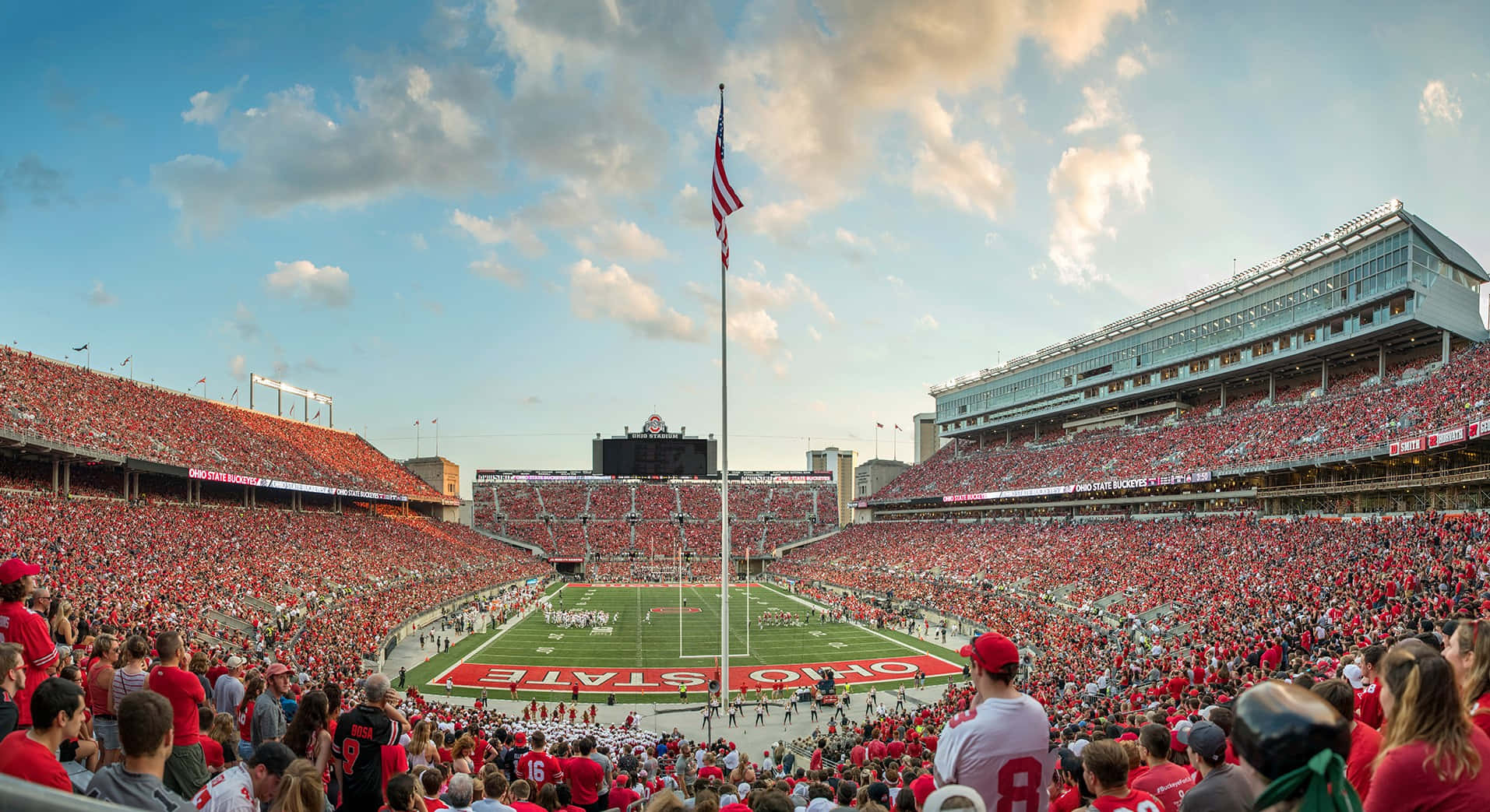 Cool Ohio State 桌布 壁紙 — 一個擠滿人的俄亥俄州立大學美式足球場，沐浴在金色的夕陽光中，身穿紅衣的球迷擠滿了看台。