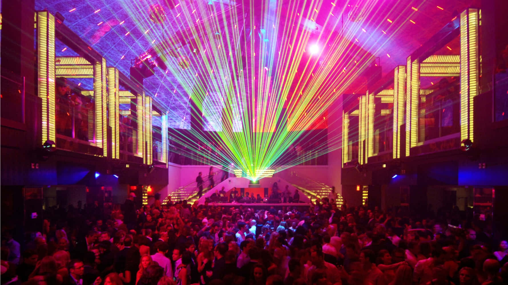 club 桌布 壁紙 — 一個擠滿人的夜總會隨著從中央舞台射向鏡面天花板和發光黃色柱子的鮮豔雷射光束而脈動。