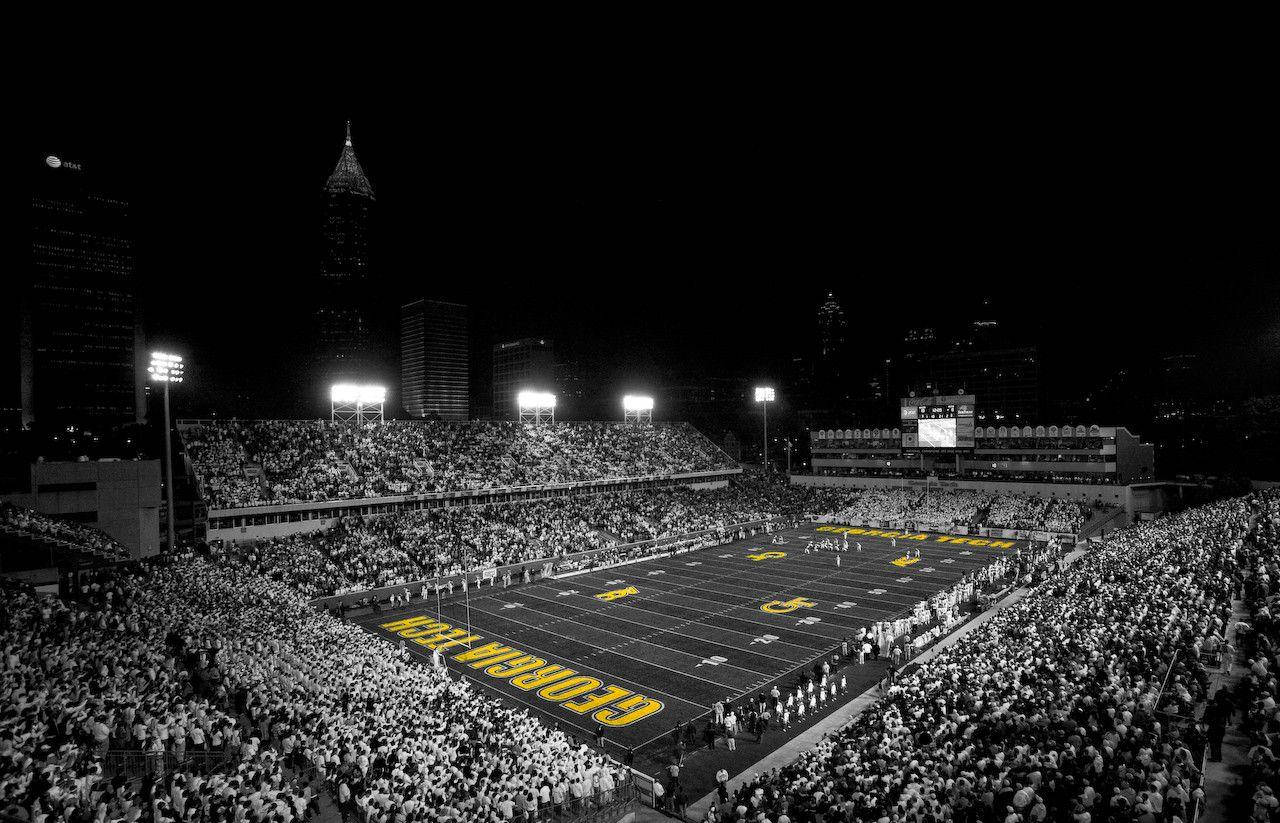 Football Field 桌布 壁紙 — 一個擠滿人的足球場的黑白夜景，明亮的燈光照亮球場和背景中的城市天際線。