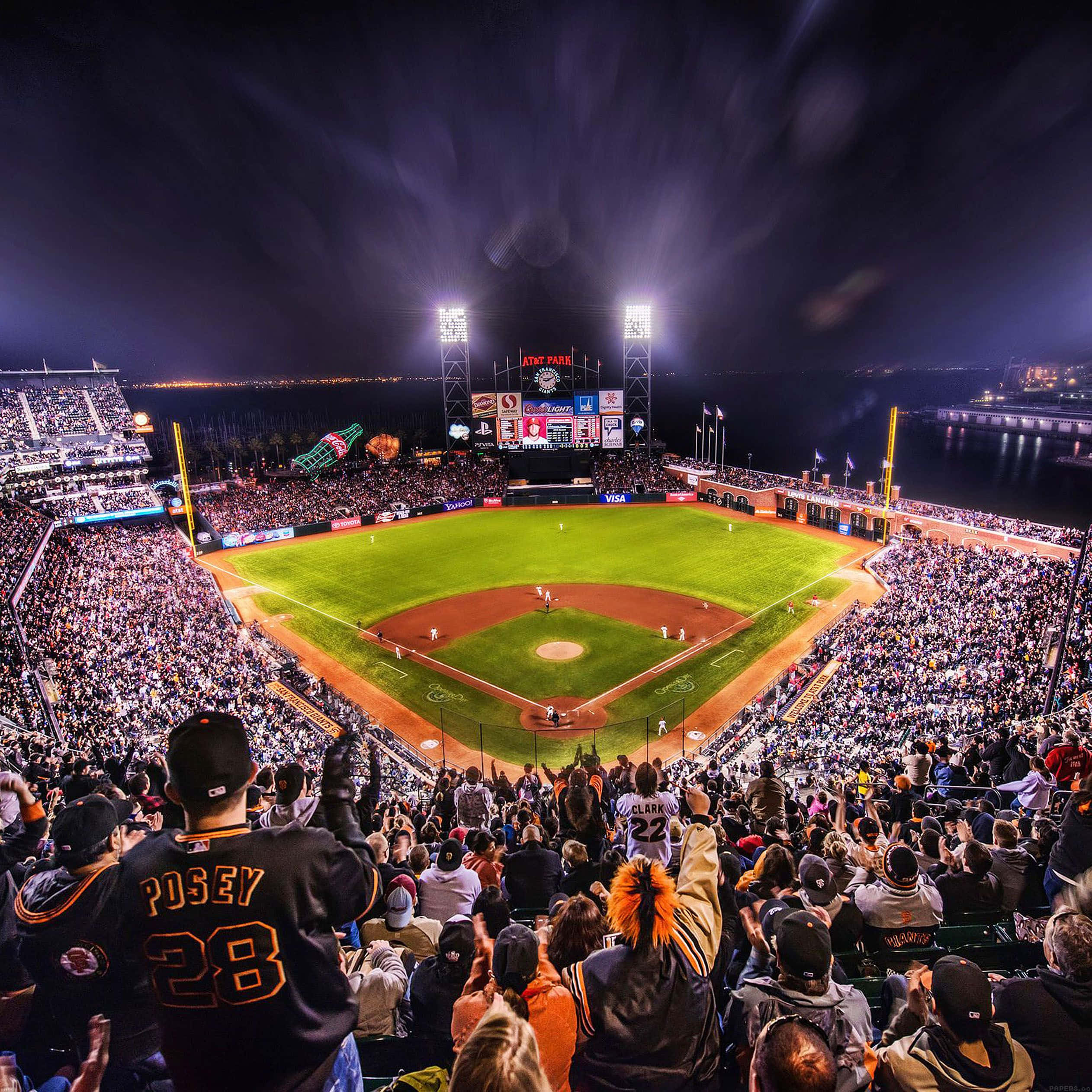 Baseball Stadium 桌布 壁紙 — 一個擠滿球迷的棒球場在夜晚，明亮的燈光下球迷歡呼，球場閃耀。