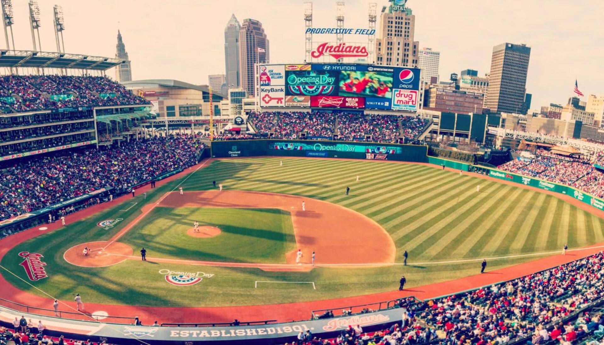 Cleveland Indians 桌布 壁紙 — 一個擠滿觀眾的棒球場的鳥瞰圖，帶有條紋綠色草地和背景的城市天際線。