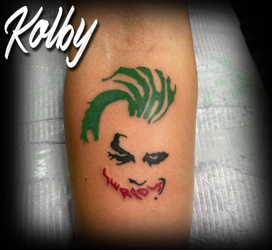 Why So Serious Joker 桌布 壁紙 — 一個新紋的Joker紋身，有綠色頭髮、黑色眼睛和紅色笑容，在一個人的前臂上。