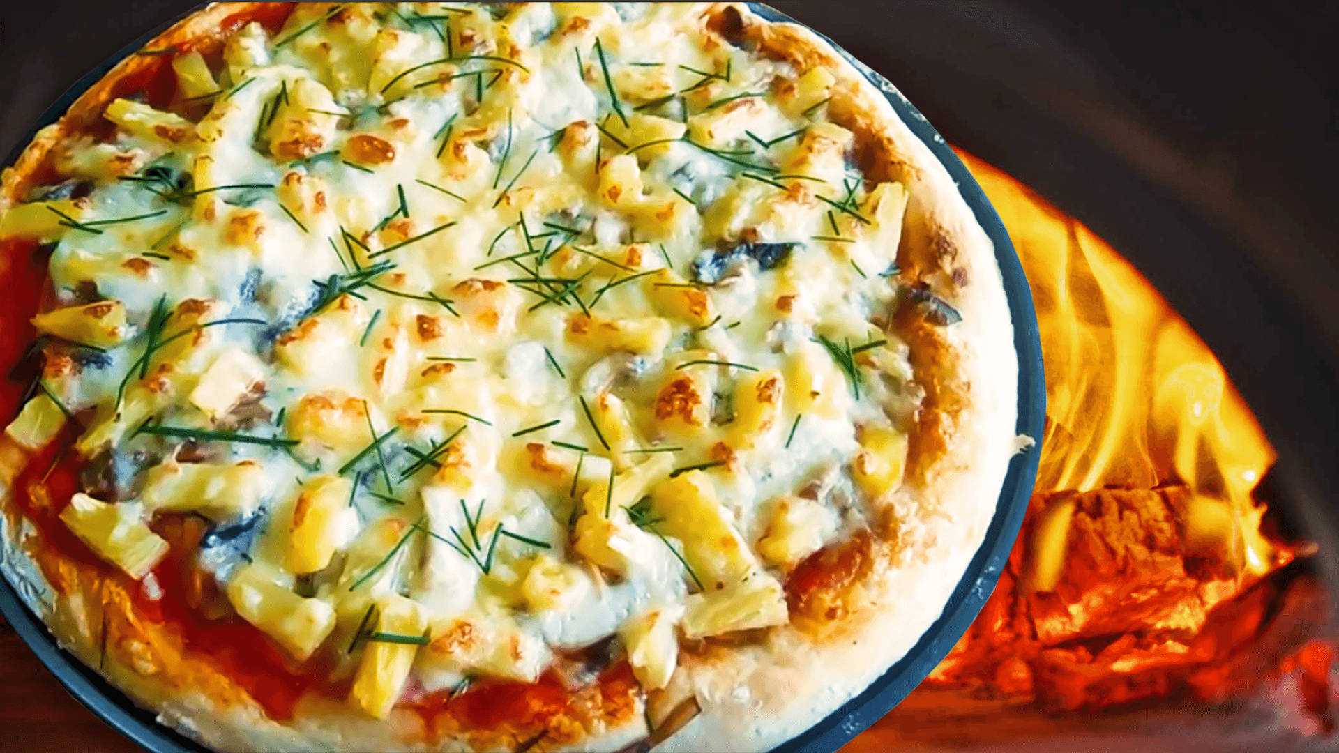 Pizza 桌布 壁紙 — 一個新鮮出爐的披薩，上面有融化的起司、鳳梨和蒔蘿，放在熱烤箱中，邊緣被發光的火焰舔舐。