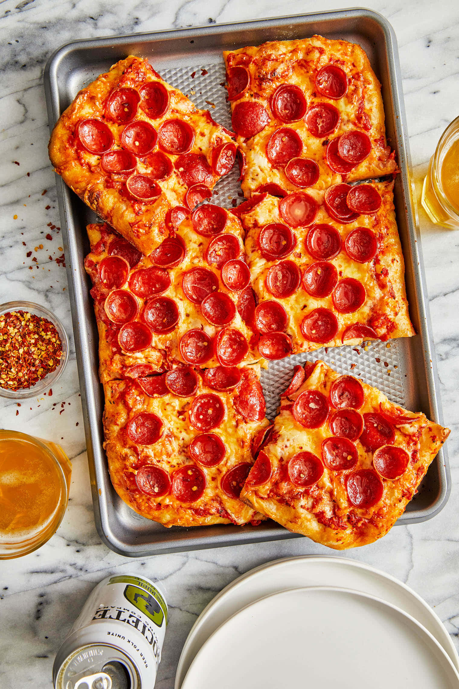 Pizza 桌布 壁紙 — 一個新鮮出爐的義大利辣味香腸披薩放在金屬托盤上，周圍有啤酒罐和紅辣椒碎，底下是大理石桌面。