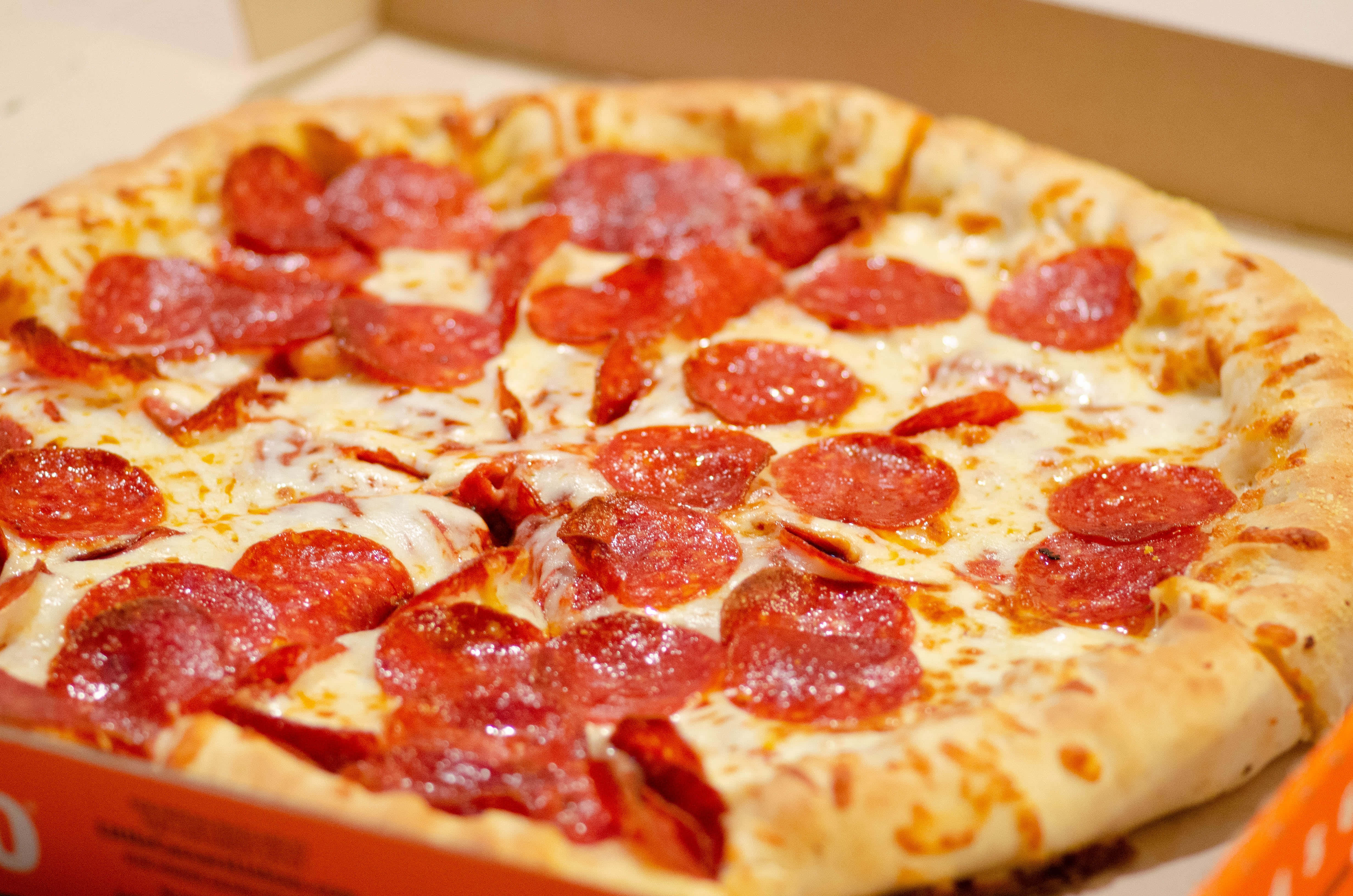 Pizza 桌布 壁紙 — 一個新鮮出爐的義大利辣香腸披薩，帶有融化的起司和酥脆的餅皮，放在一個開著的紙箱裡，非常誘人。