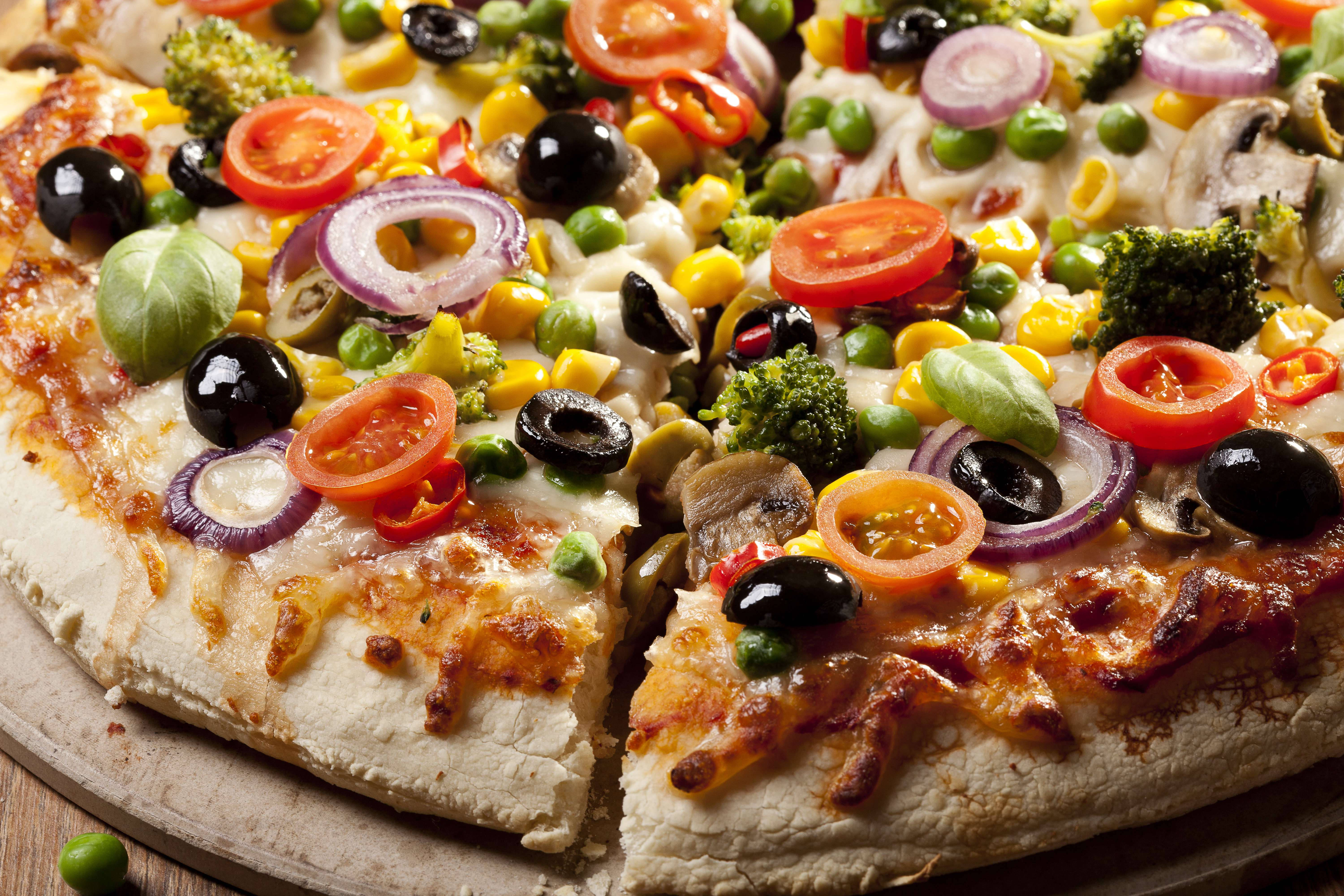 Dominos Pizza 桌布 壁紙 — 一個新鮮出爐的蔬菜披薩特寫，上面鋪滿鮮豔的櫻桃番茄、橄欖和西蘭花，放在木托盤上。