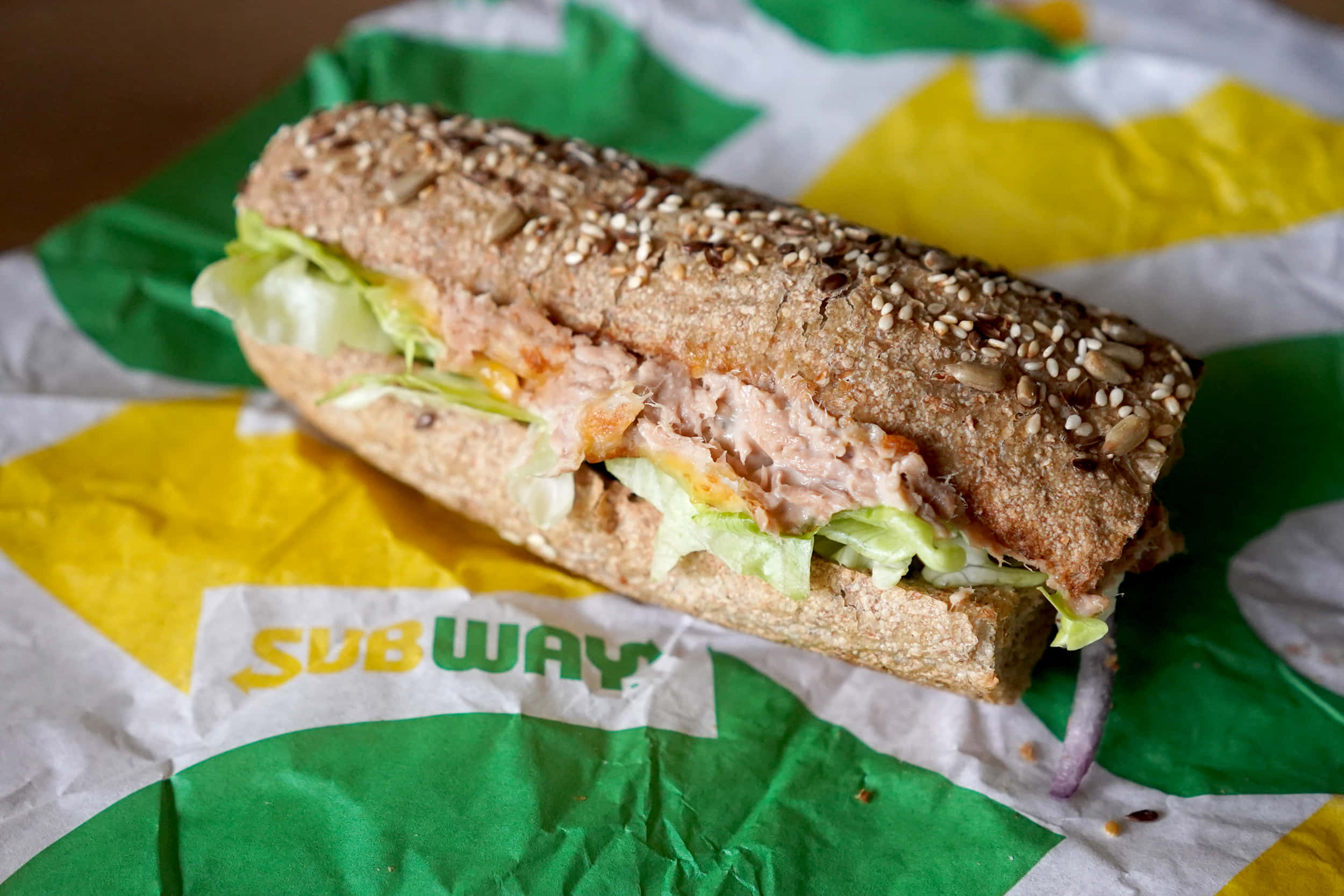 Subway 桌布 壁紙 — 一個新鮮製作的Subway三明治，配芝麻麵包和鮪魚沙拉，放在品牌紙上。