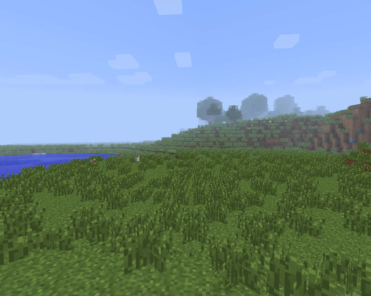 桌布 壁紙 — 一個方塊狀的Minecraft景觀，有綠色草山丘、藍色河流和遠處的樹木，天空晴朗。