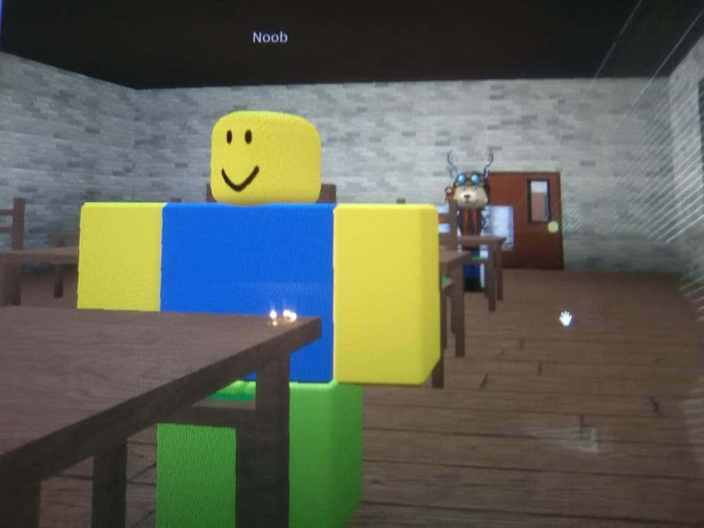 Roblox Noob 桌布 壁紙 — 一個方塊狀的黃藍色頭像，面帶微笑，坐在一張木桌旁，房間光線昏暗，有磚牆，背景中還有另一個角色。