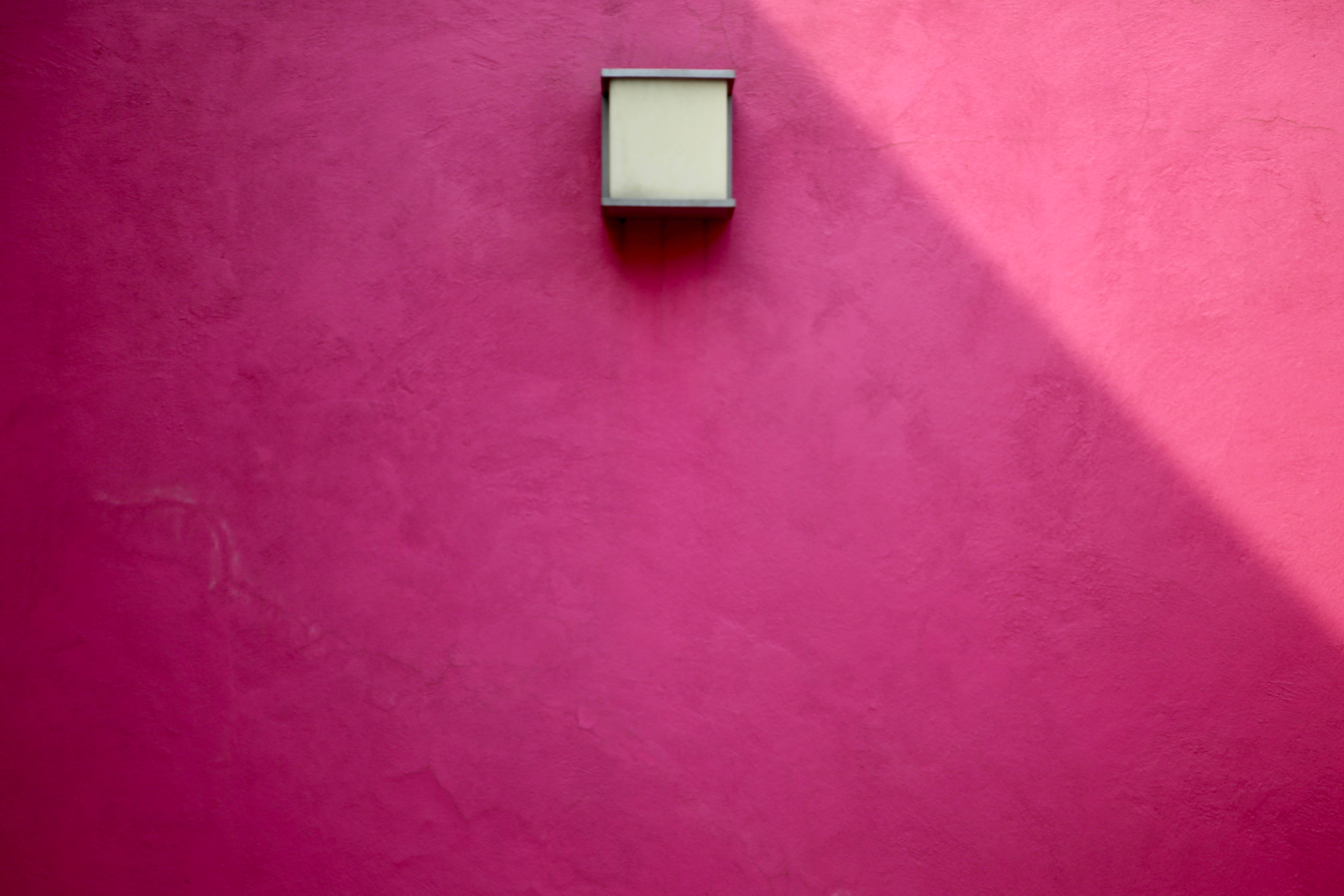 Pink Wall 桌布 壁紙 — 一個方形壁掛式燈具在明亮的陽光下，在充滿活力的紋理粉紅色牆壁上投射出清晰的陰影。
