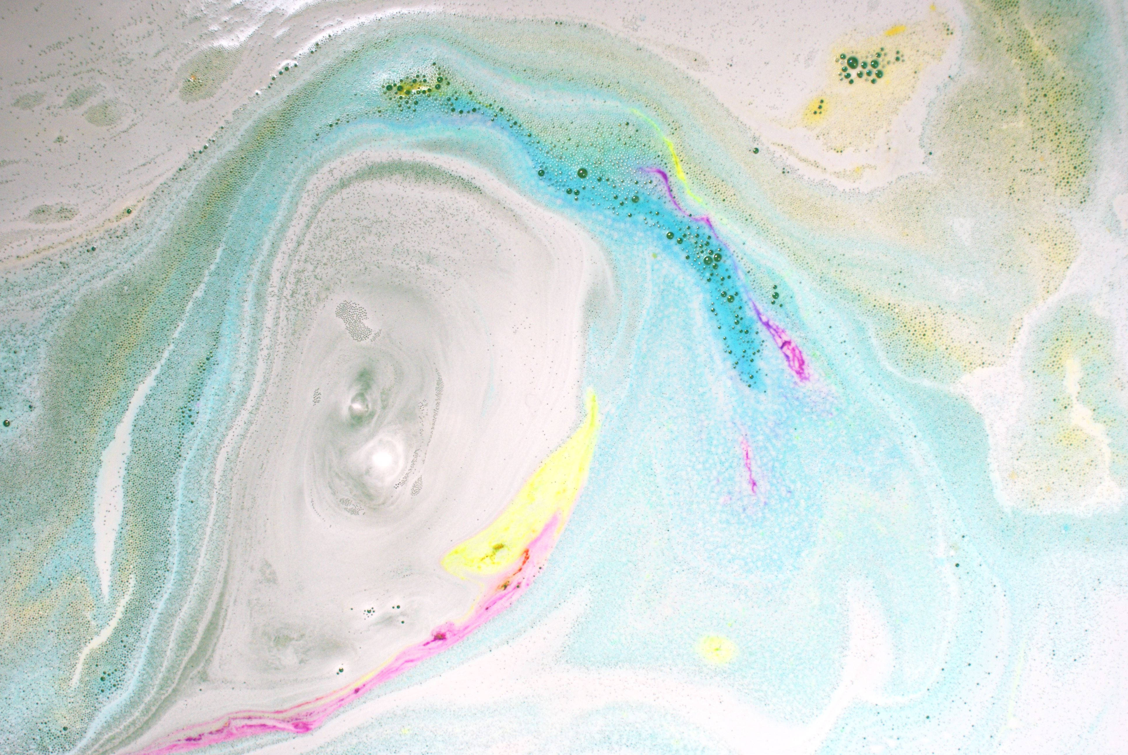 Lush 桌布 壁紙 — 一個旋轉的抽象圖案，包含粉藍、粉黃和粉紅，帶有斑點紋理和流動感。