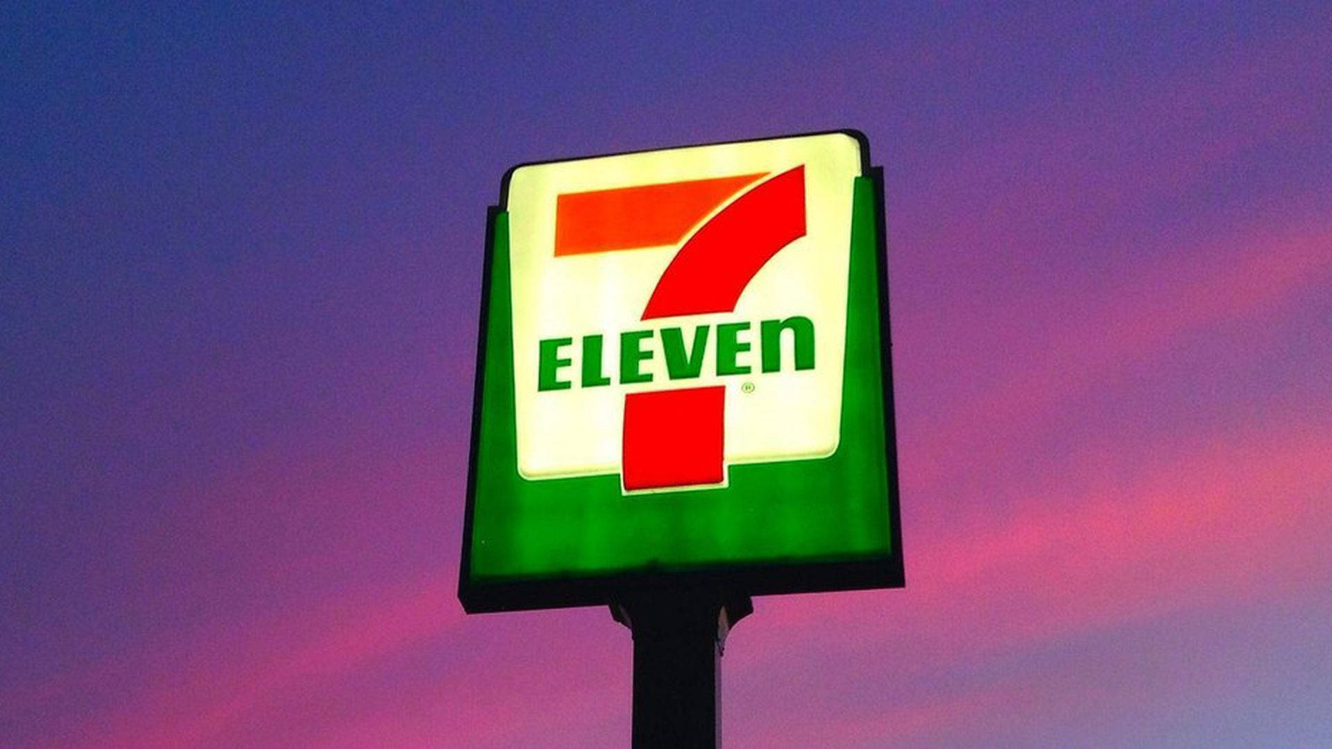 Eleven 桌布 壁紙 — 一個明亮照明的7-Eleven標誌在紫色和粉紅色雲彩繪成的暮色天空中發光。