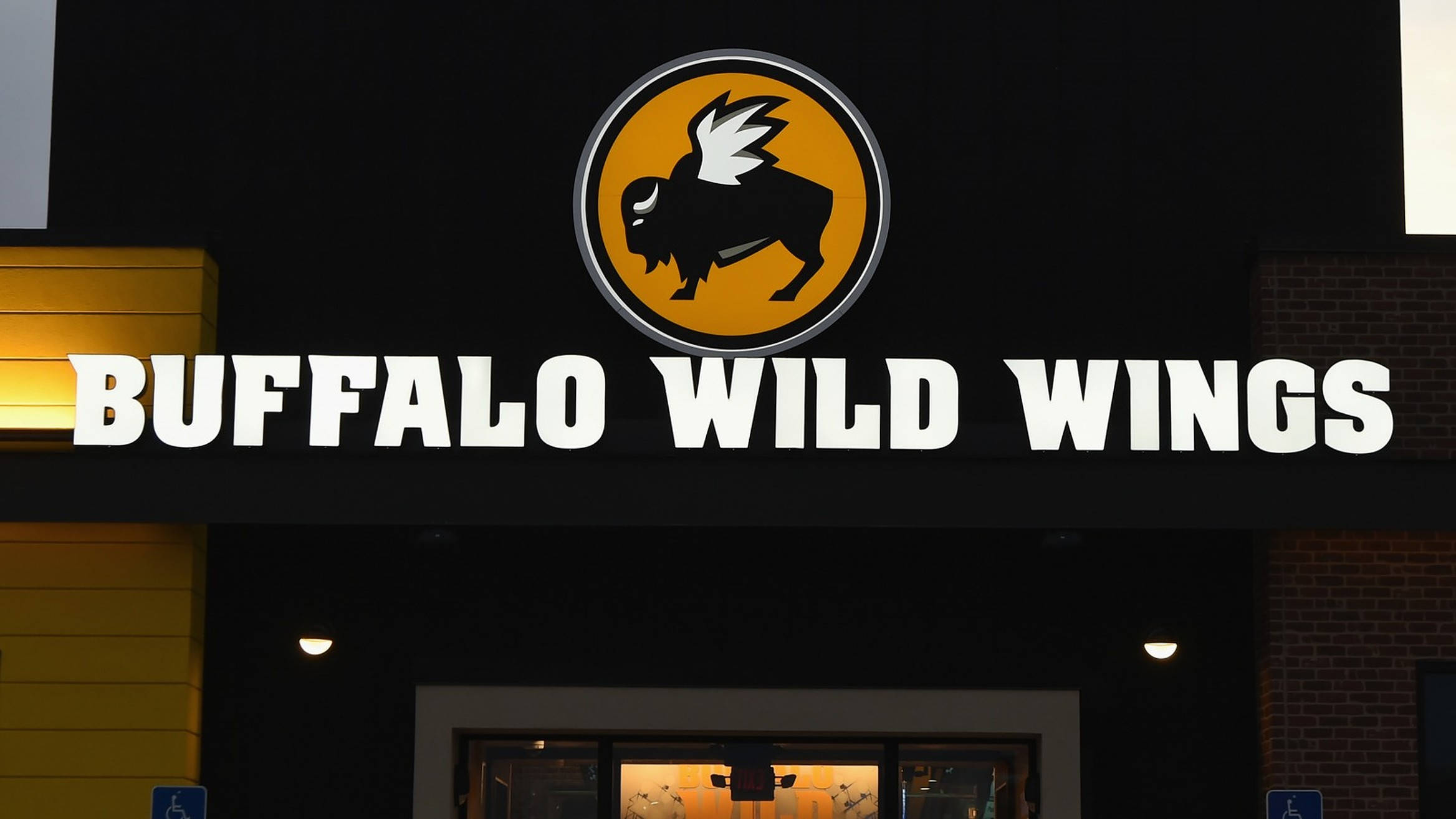 Wild 桌布 壁紙 — 一個明亮照明的Buffalo Wild Wings餐廳招牌，在深色外牆上有一個黃色圓圈，上面有一隻帶翅膀的黑色水牛。