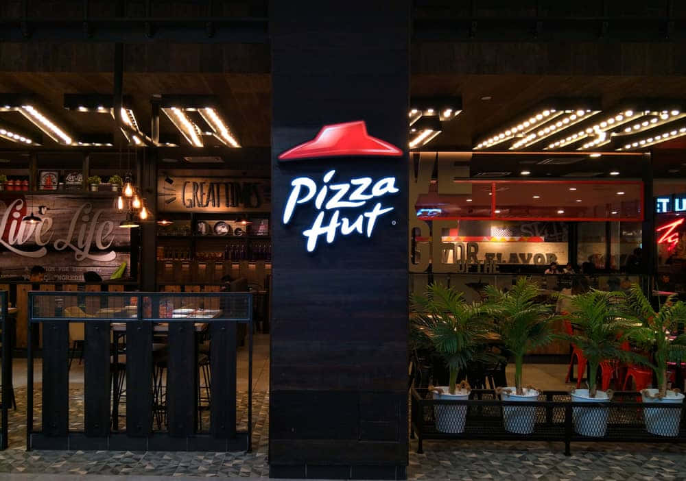 夜晚的Pizza Hut餐廳入口，帶有發光標誌和盆栽植物。 — 必勝客 壁紙