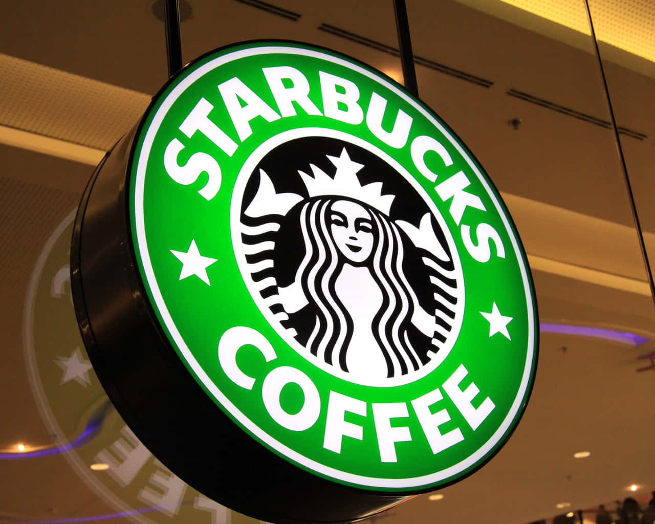 星巴克 桌布 壁紙 — 一個明亮照明的Starbucks咖啡標誌牌掛在室內，發出綠色光芒，帶有白色文字和人魚標誌。