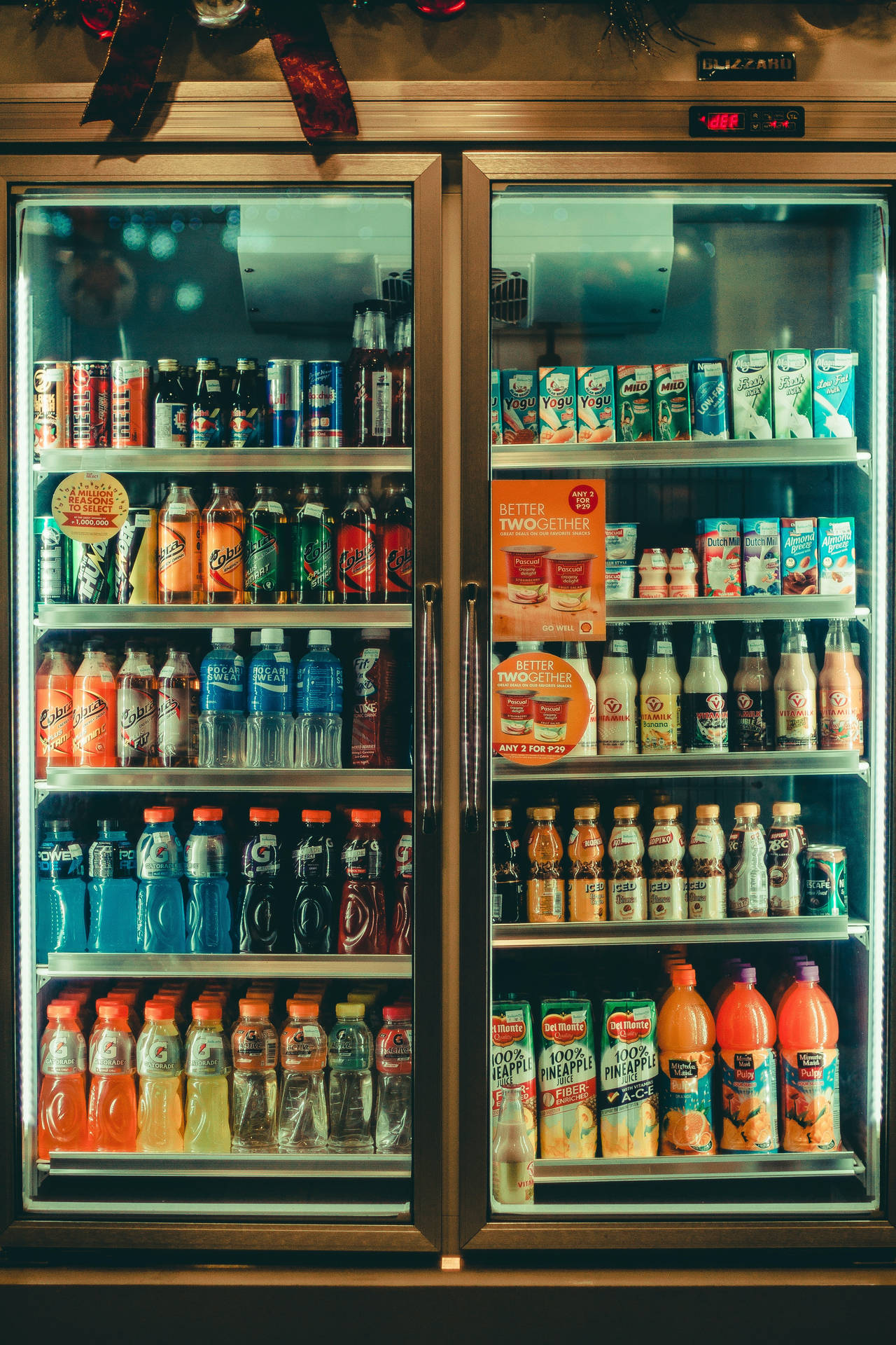 Drink 桌布 壁紙 — 一個明亮照明的雙門飲品冰箱，在溫暖的環境燈光下裝滿了色彩繽紛的汽水、果汁和飲料。