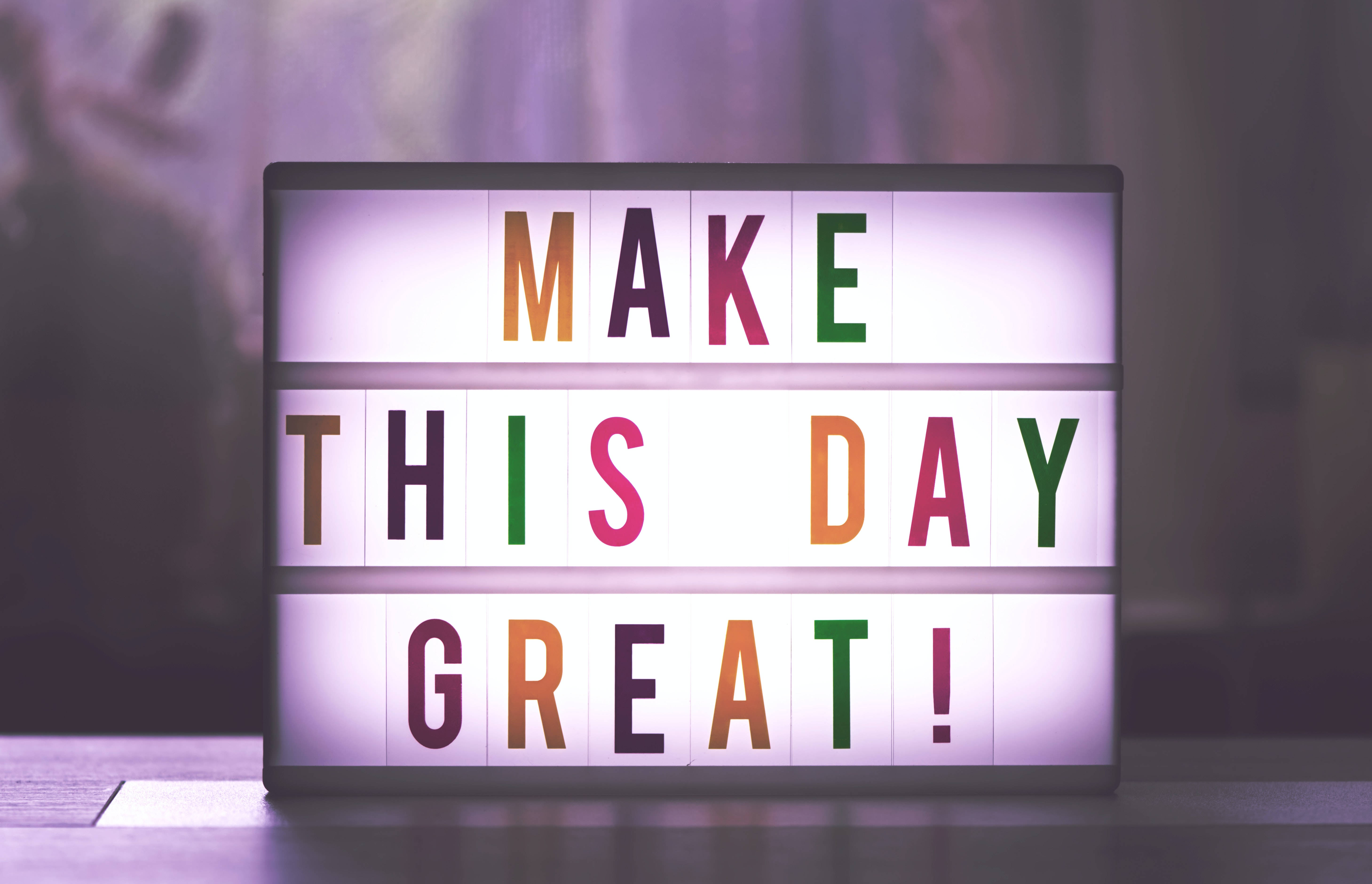 Inspirational Quotes 桌布 壁紙 — 一個明亮發光的招牌，彩色字母拼出「MAKE THIS DAY GREAT!」，在柔和的紫色模糊背景上閃耀。
