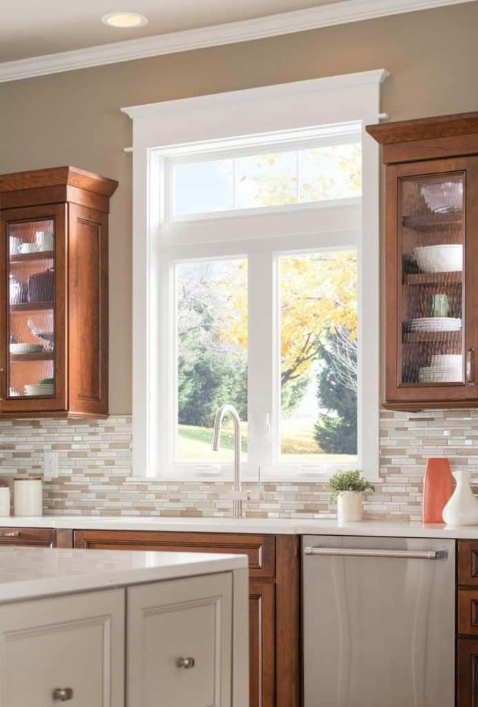 Kitchen Design 桌布 壁紙 — 一個明亮的廚房，配有木製櫥櫃和瓷磚防濺板，俯瞰著一扇窗戶，窗外是金黃色葉子的秋樹。