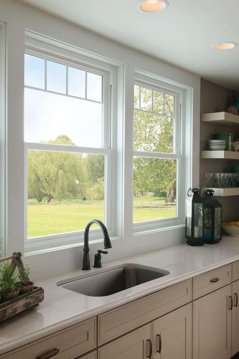 Kitchen Design 桌布 壁紙 — 一個明亮的廚房，配有白色櫥櫃和水槽，透過大窗戶可以俯瞰一片鬱鬱蔥蔥的綠色田野和垂柳。