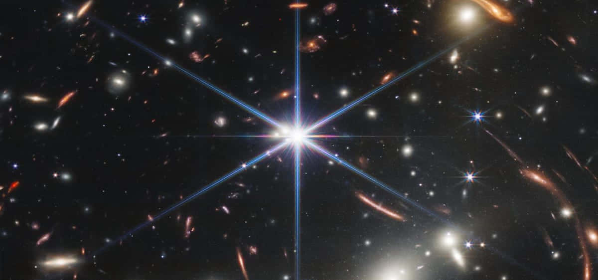 Stars 桌布 壁紙 — 一個明亮的星暴星系在充滿遙遠星系和恆星的黑暗宇宙場中散發出強烈的藍光。