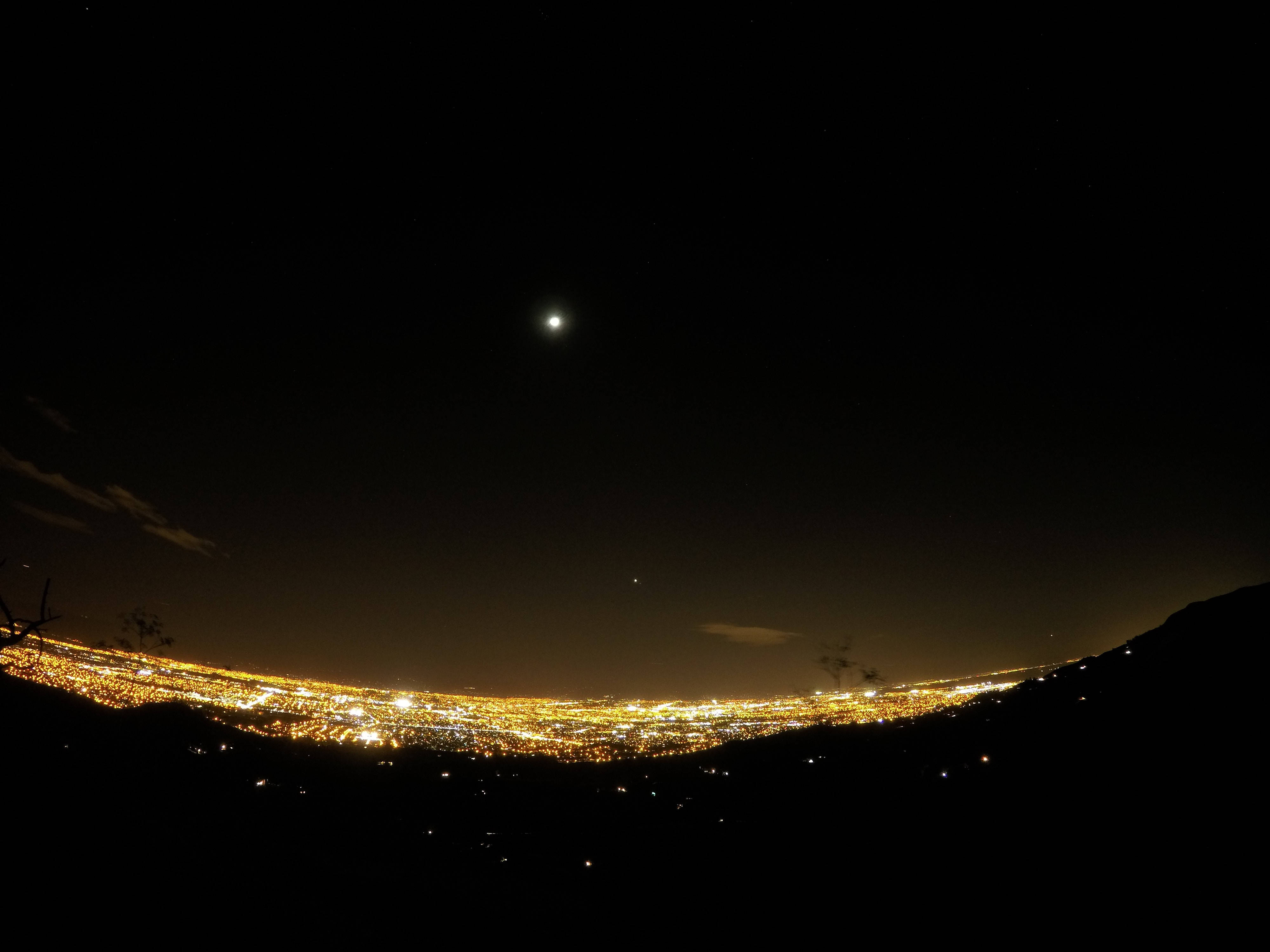 夜空 桌布 壁紙 — 一個明亮的月亮照耀著山谷中一座廣闊城市的全景夜景。