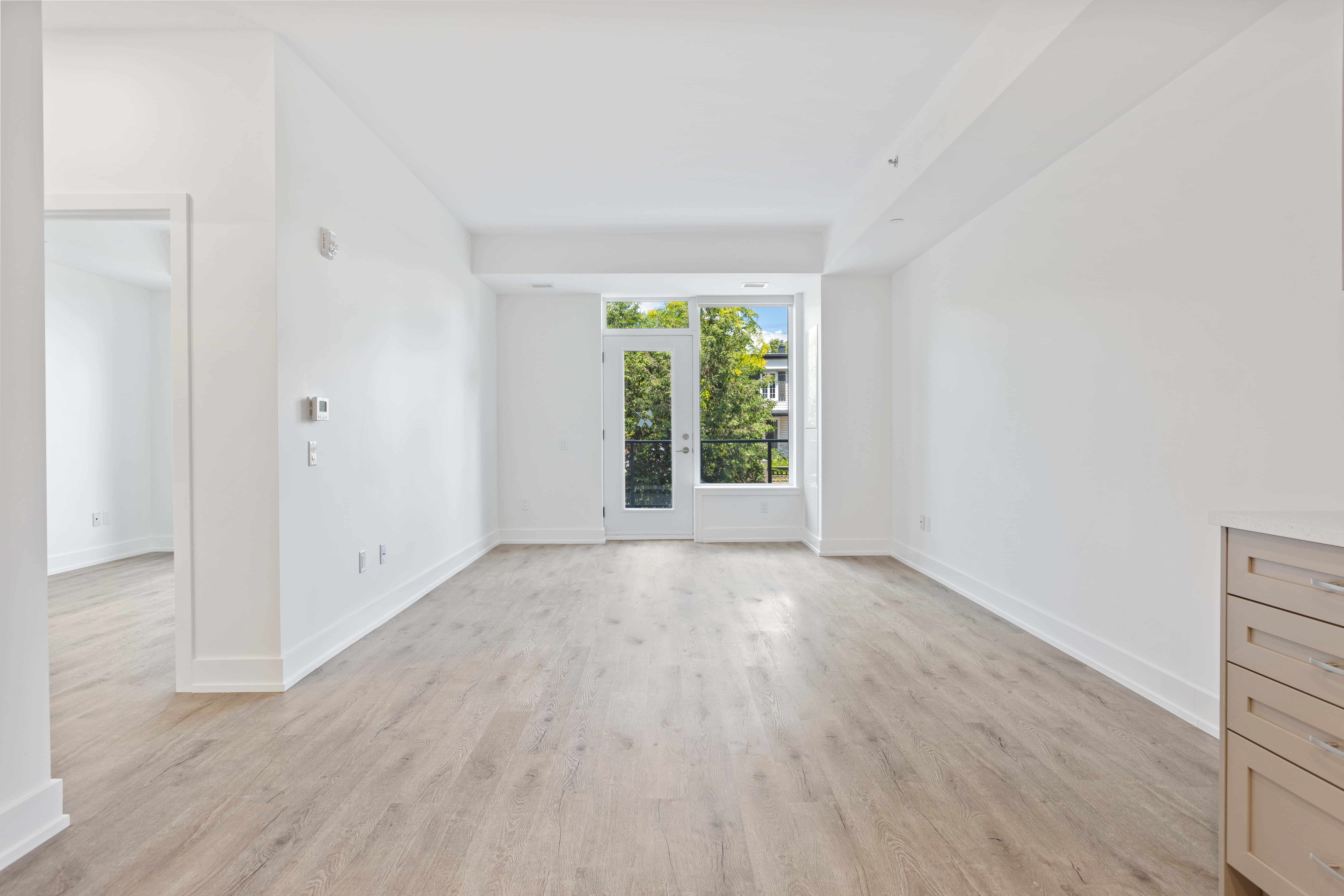 Empty Room 桌布 壁紙 — 一個明亮的極簡房間，鋪有淺色木地板和白色牆壁，設有通往綠意的玻璃門。