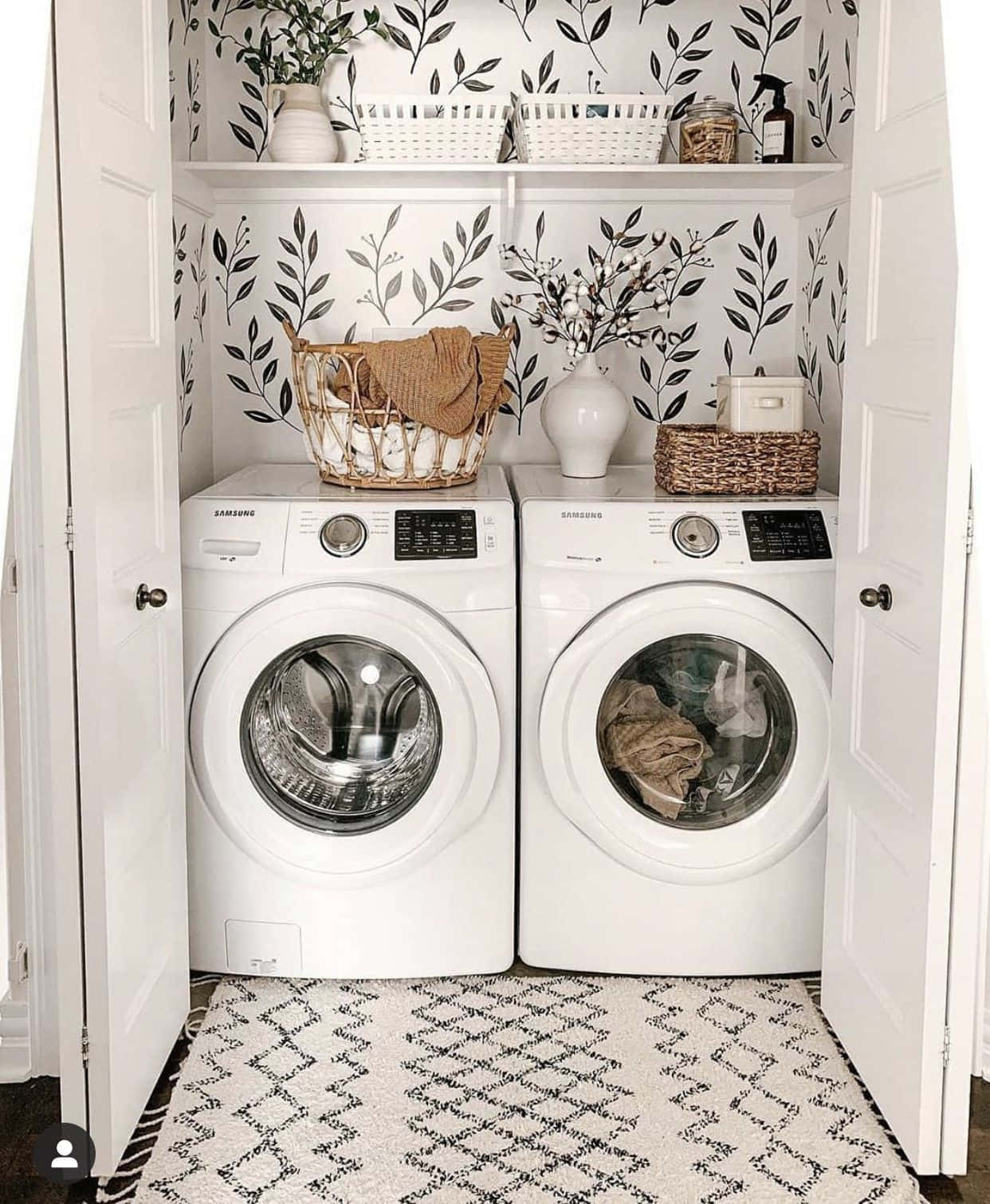 Laundry Room 桌布 壁紙 — 一個明亮的洗衣角落，配有白色前置式洗衣機、黑色葉紋壁紙，以及裝有毛巾和裝飾品的編織籃。