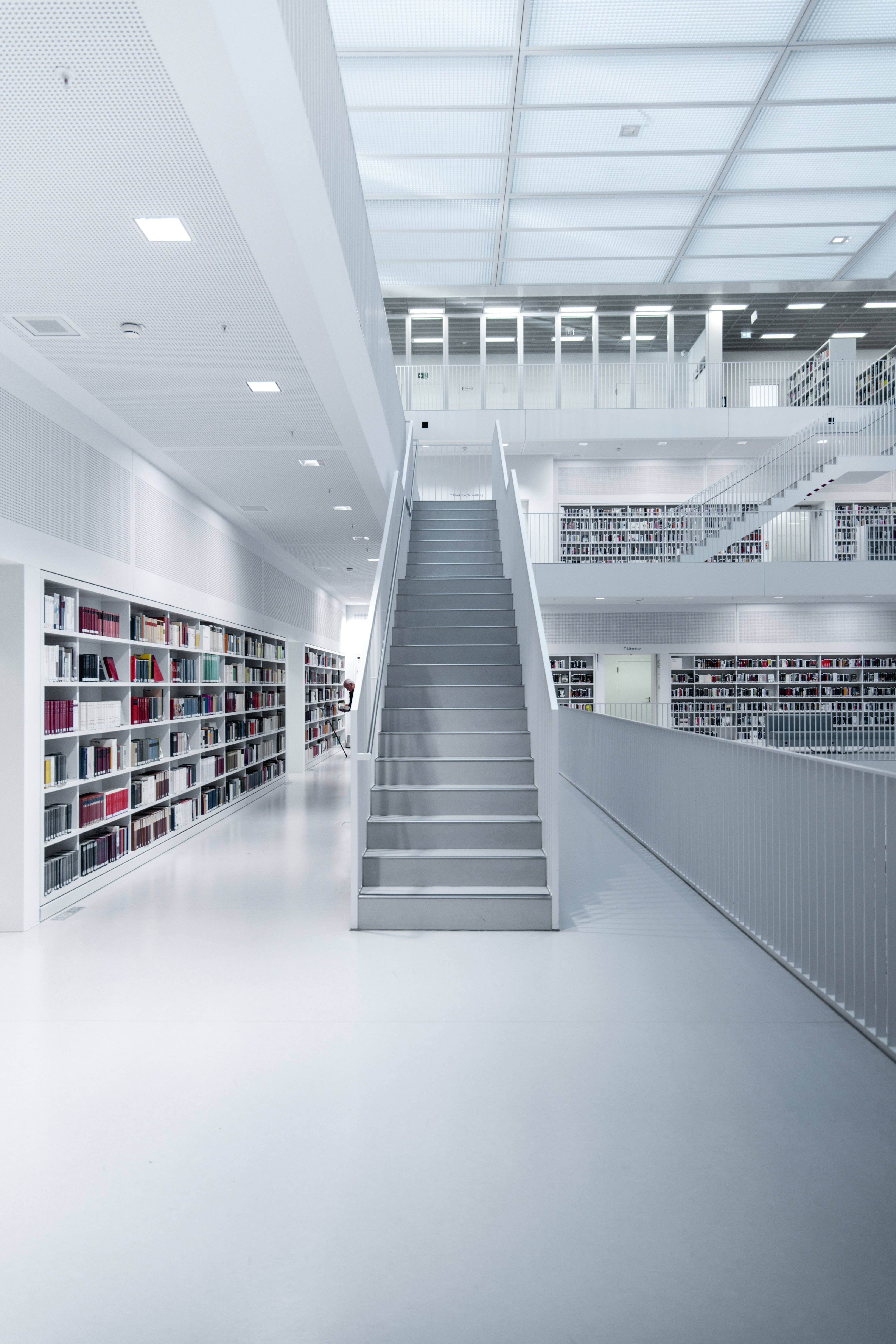 Library 桌布 壁紙 — 一個明亮的現代圖書館，設有白色牆壁、書架和通往樓上的中央樓梯。