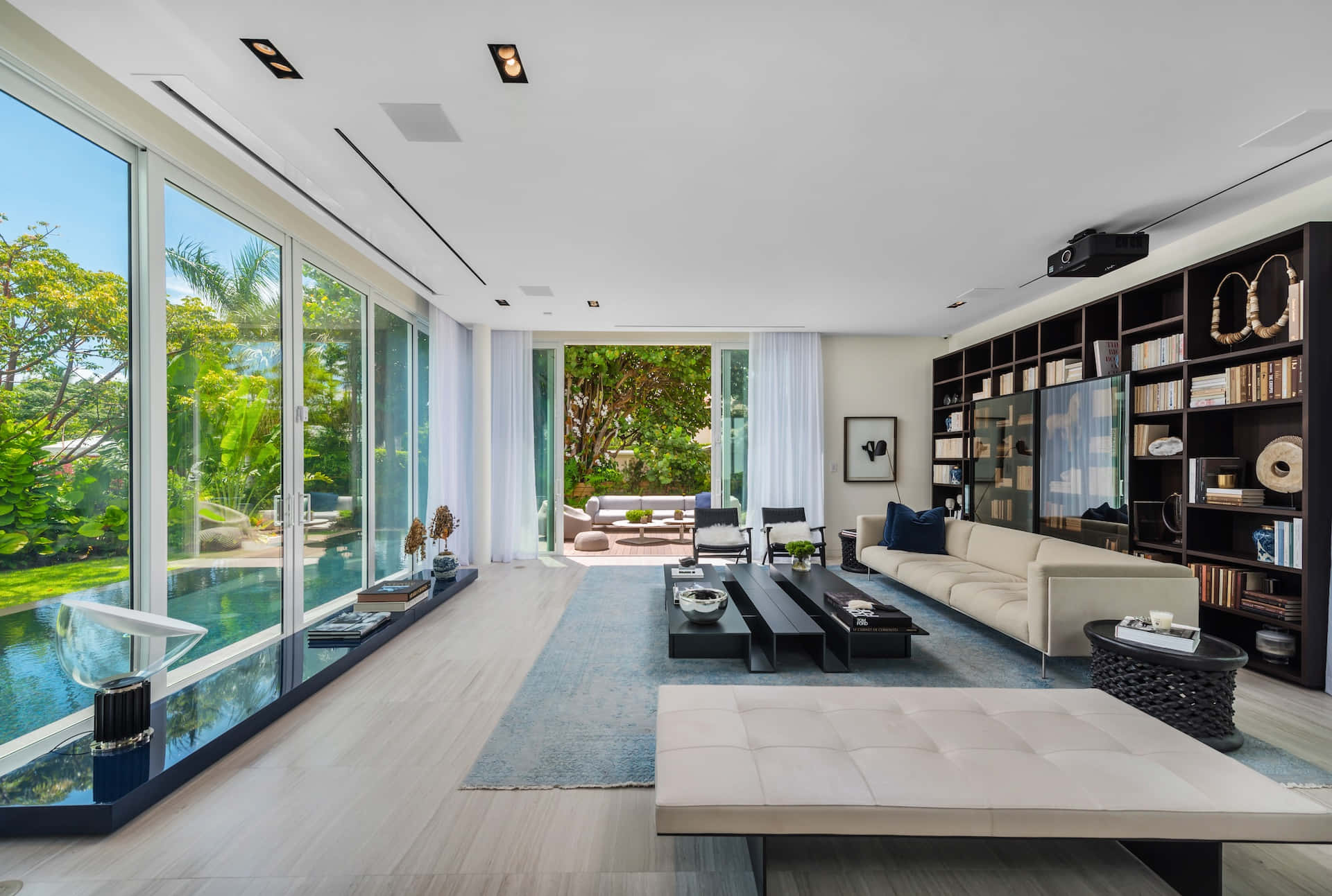 Minimalist Architecture 桌布 壁紙 — 一個明亮的現代客廳，設有落地玻璃牆，可俯瞰鬱鬱蔥蔥的花園和游泳池。
