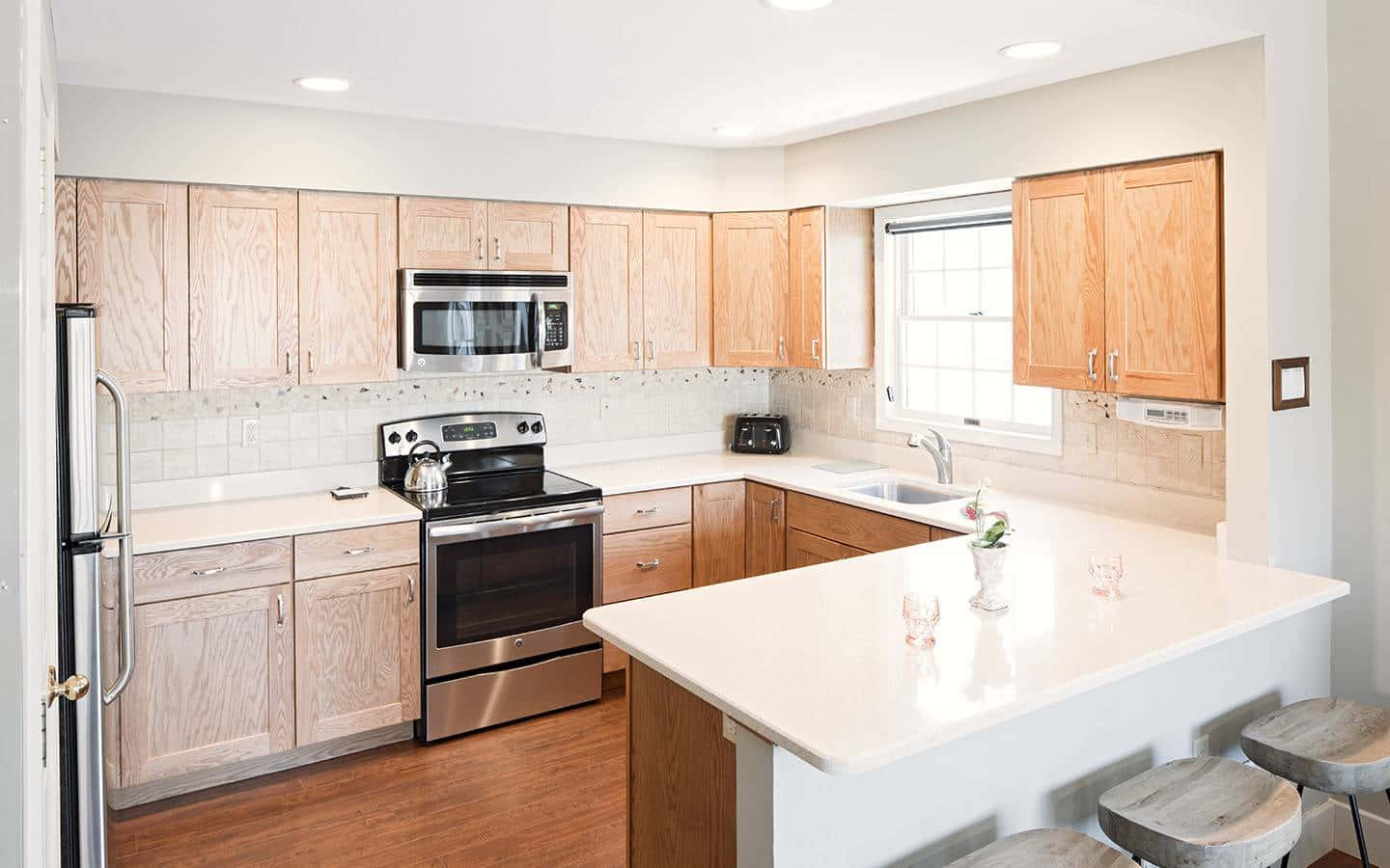 1440p Kitchen 桌布 壁紙 — 一個明亮的現代廚房，配有淺色木櫃、不鏽鋼電器，以及一個在柔和自然光下的白色中島。