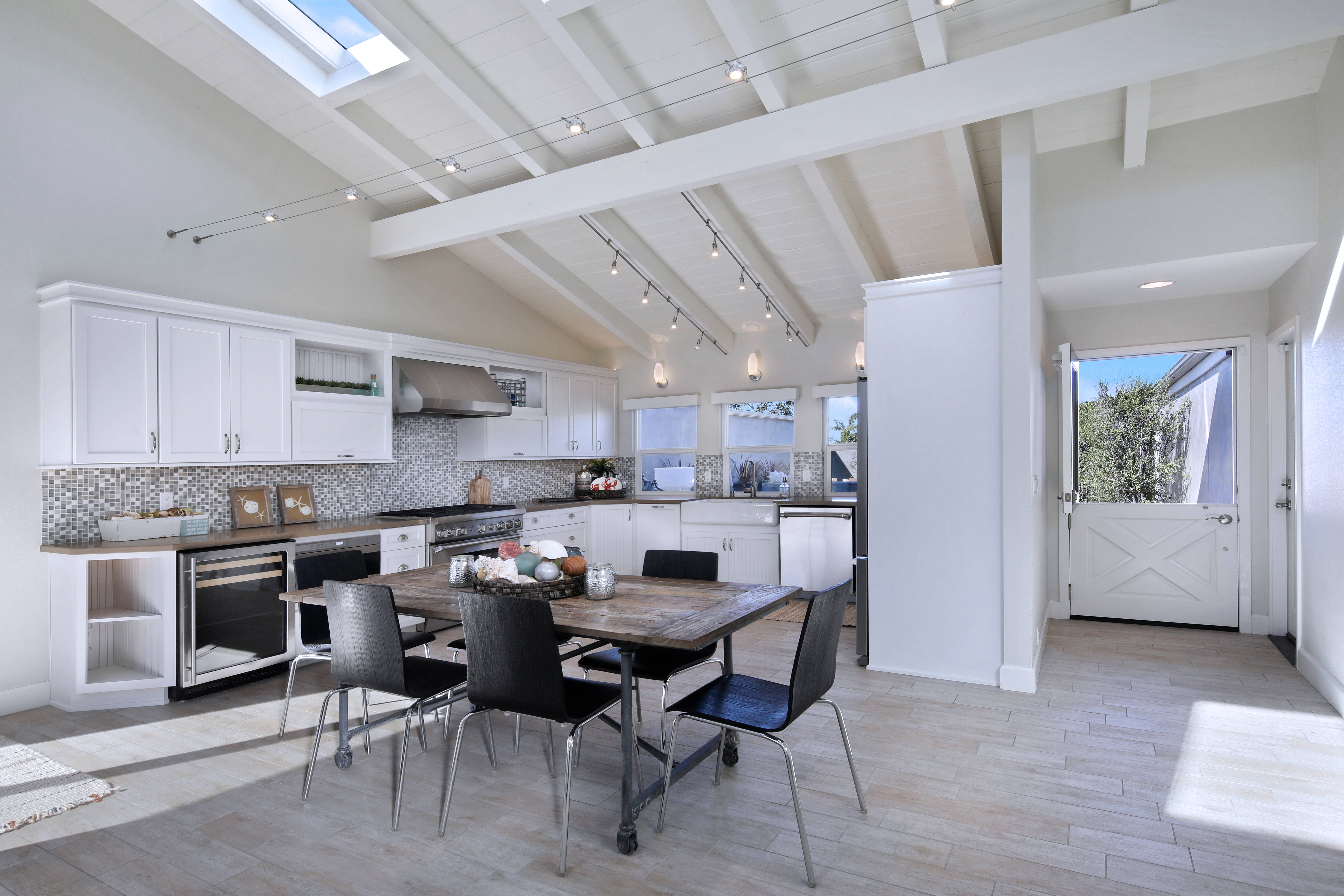 Interior Design 桌布 壁紙 — 一個明亮的現代廚房，配有白色櫥櫃和裸露的橫樑，在天窗和軌道燈光下有一張木製餐桌，周圍環繞著黑色椅子。