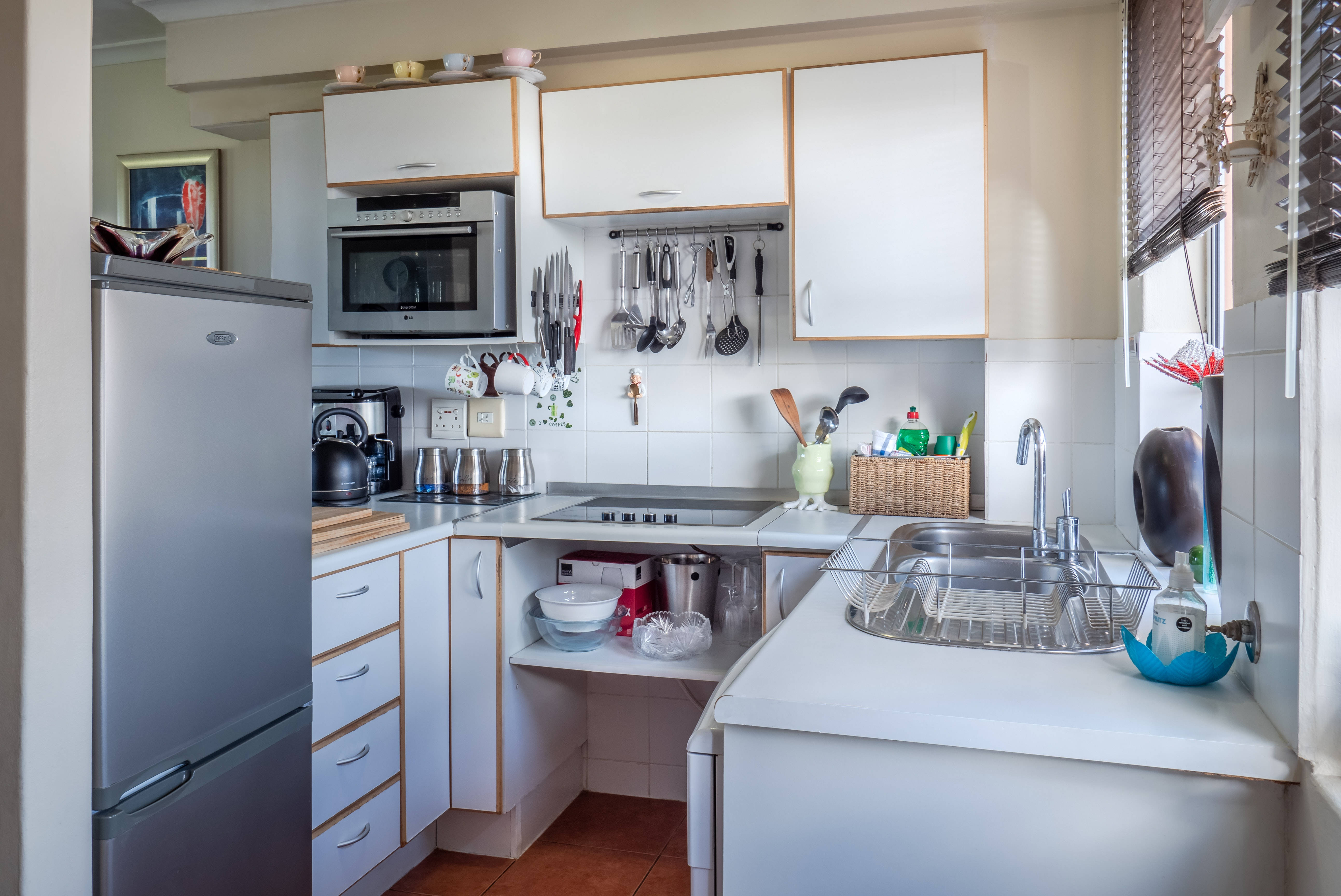 kitchen 桌布 壁紙 — 一個明亮的現代廚房，配有白色櫥櫃、不鏽鋼電器，以及來自帶百葉窗窗戶的自然光。