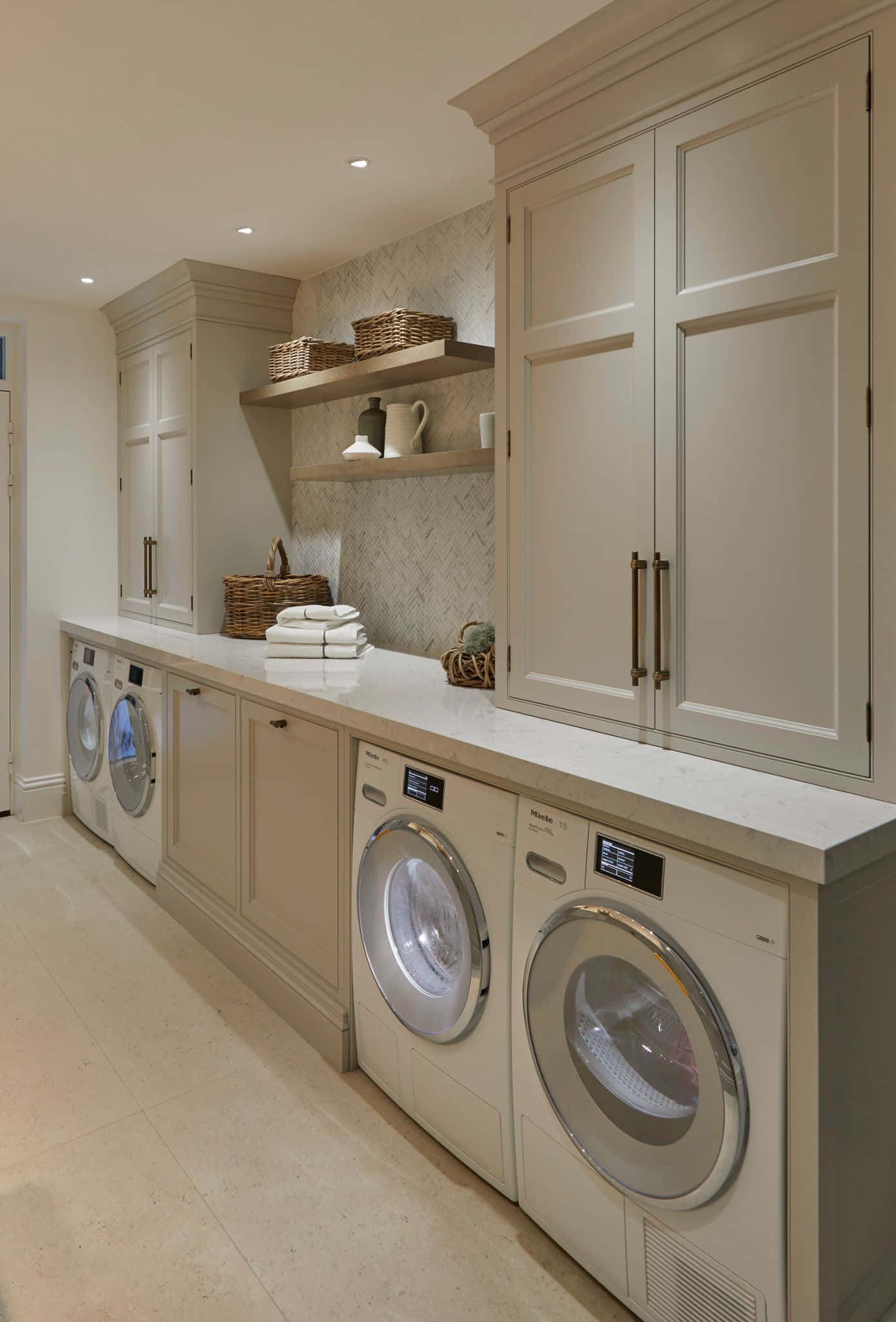 Laundry Room 桌布 壁紙 — 一個明亮的現代洗衣房，配有奶油色櫥櫃、大理石檯面，以及在溫暖嵌入式燈光下堆疊的前置式洗衣機和乾衣機。