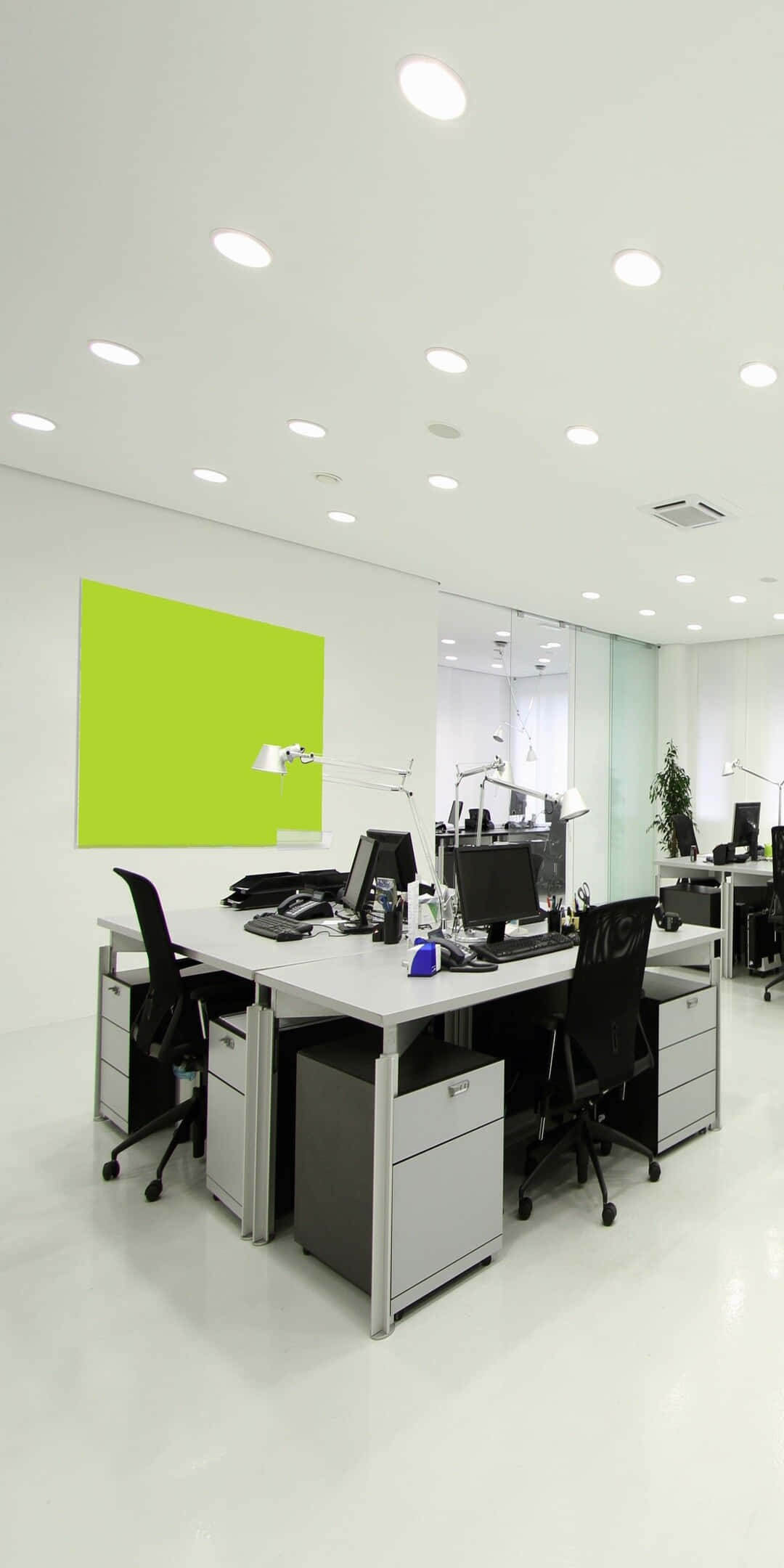 Pixel 3 Office 桌布 壁紙 — 一個明亮的現代辦公室，配有白色辦公桌、黑色椅子，以及在嵌入式天花板燈下的充滿活力的萊姆綠色特色牆。