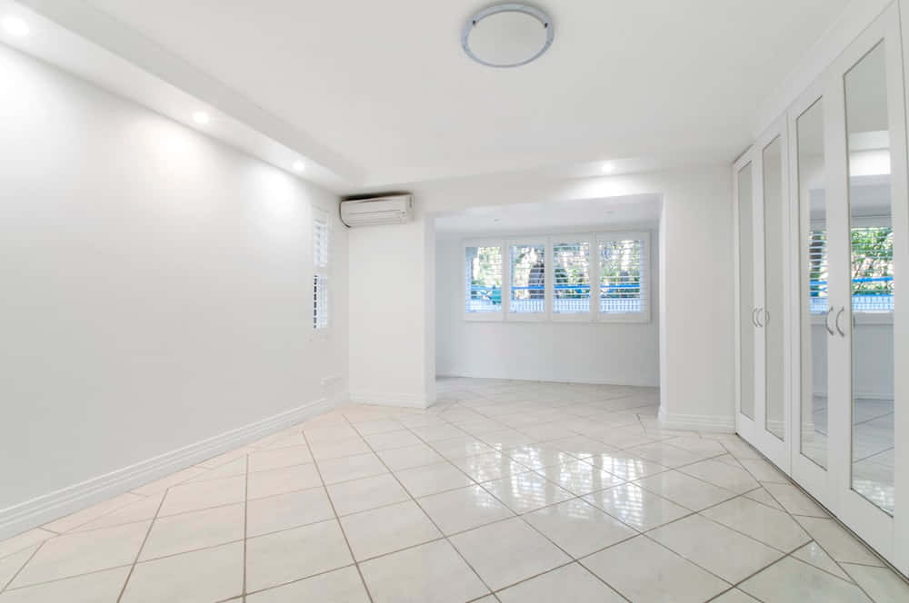 Empty Room 桌布 壁紙 — 一個明亮的空房間，白色牆壁、瓷磚地板和鏡面衣櫃門反射出外面的綠色植物。