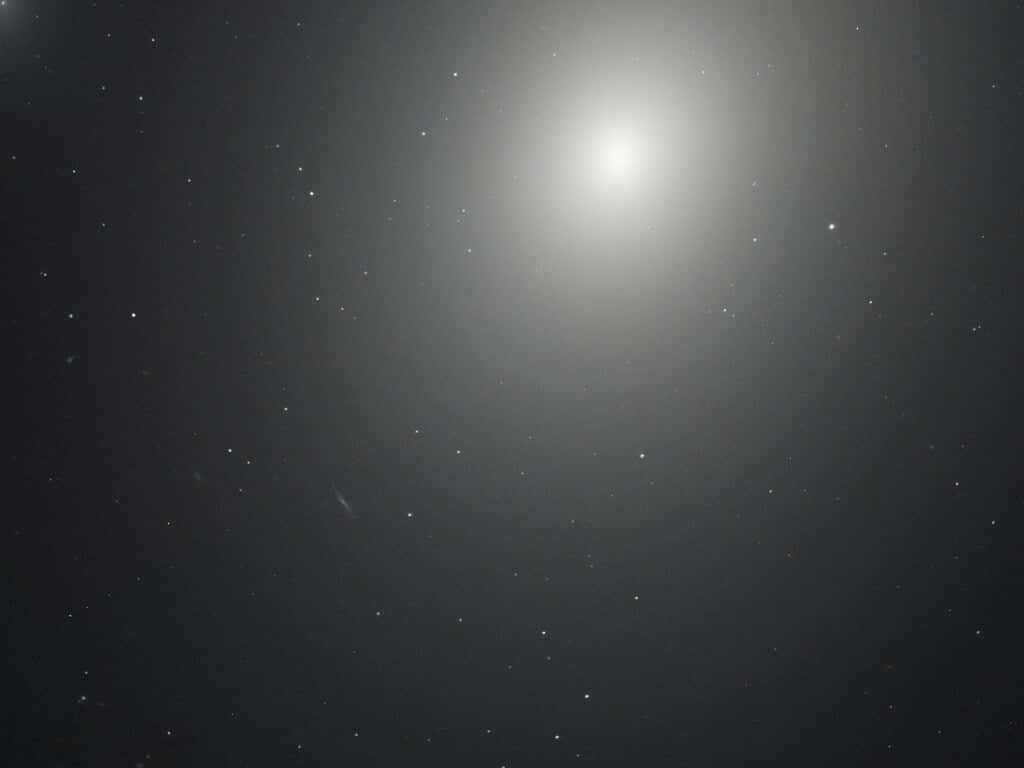 Elliptical Galaxy 桌布 壁紙 — 一個明亮的螺旋星系主宰著一個帶有柔和漸變和散落光點的星場。