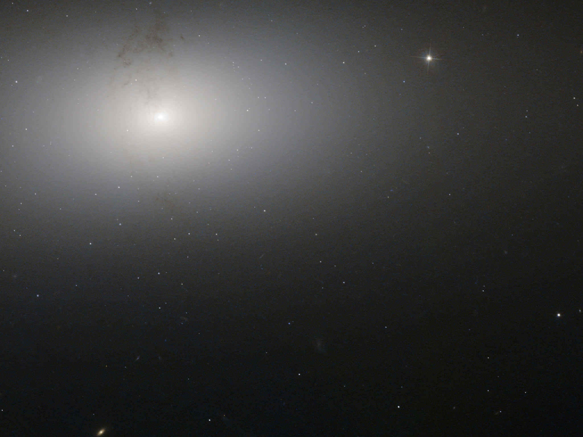 Elliptical Galaxy 桌布 壁紙 — 一個明亮的螺旋星系在佈滿星星的宇宙虛空中柔和地發光，附近有一顆明亮的星星閃耀。