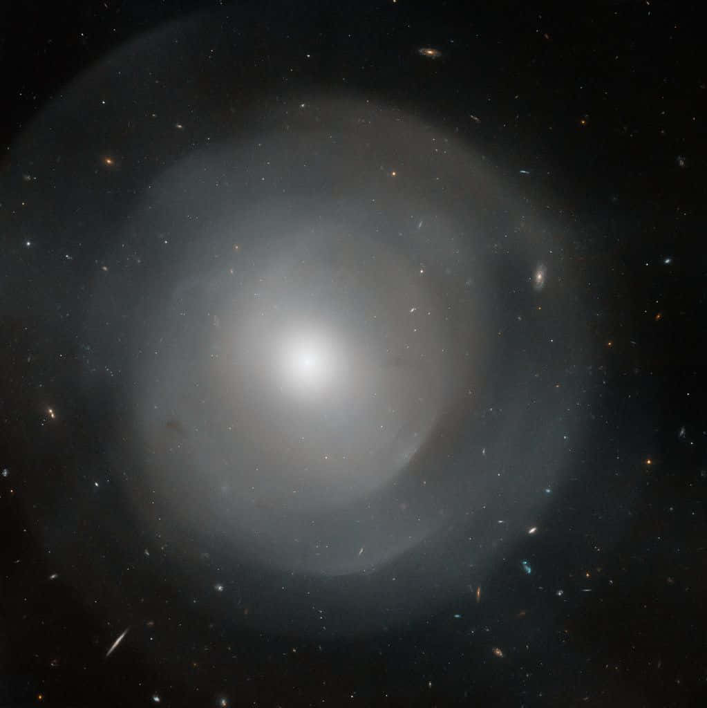 Elliptical Galaxy 桌布 壁紙 — 一個明亮的螺旋星系在充滿遙遠星系和宇宙塵埃的星場中心發光。
