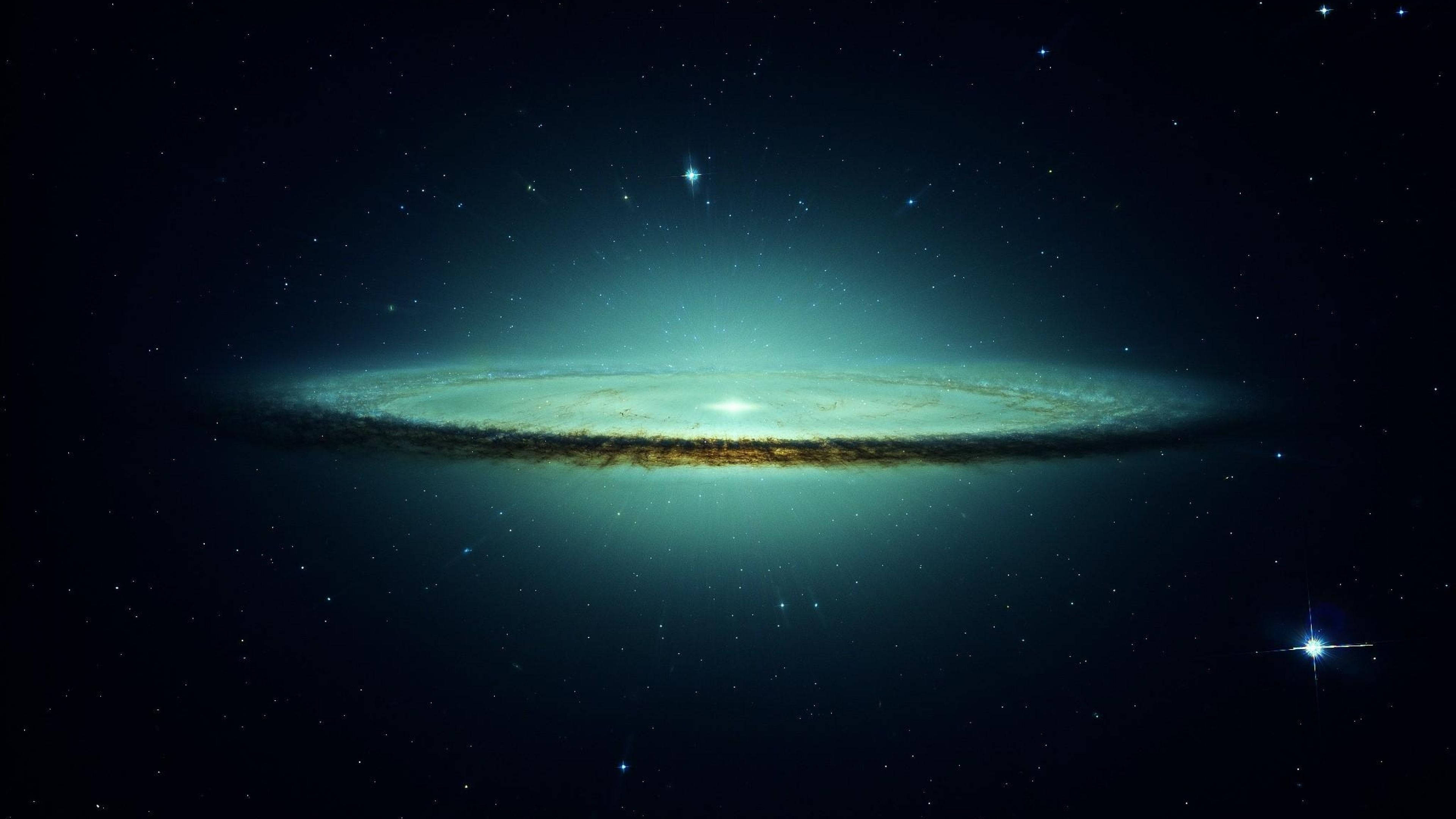 4K 太空 桌布 壁紙 — 一個明亮的螺旋星系在星空背景下散發著藍綠色和金色的光芒。