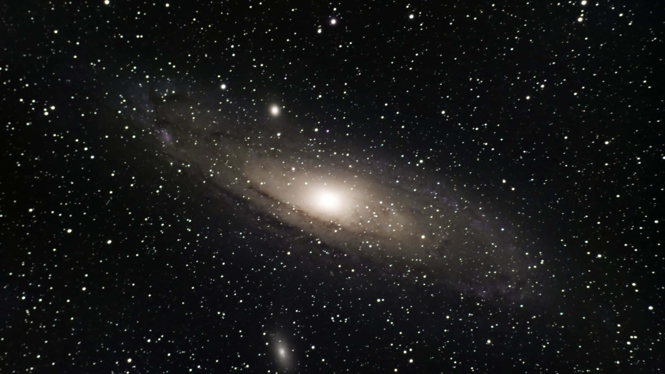 2160x1215 桌布 壁紙 — 一個明亮的螺旋星系在深空的星場中發光，帶有明亮的核心和旋轉的旋臂。