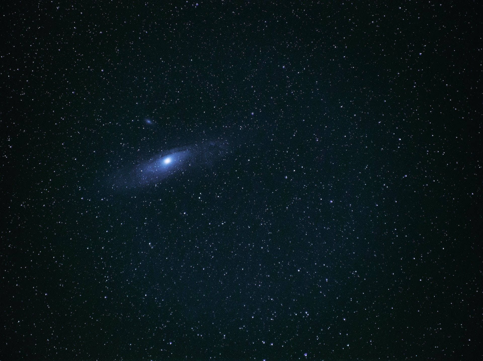 夜空 桌布 壁紙 — 一個明亮的螺旋星系在深邃宇宙之夜中，以無數恆星為背景，柔和地發光。