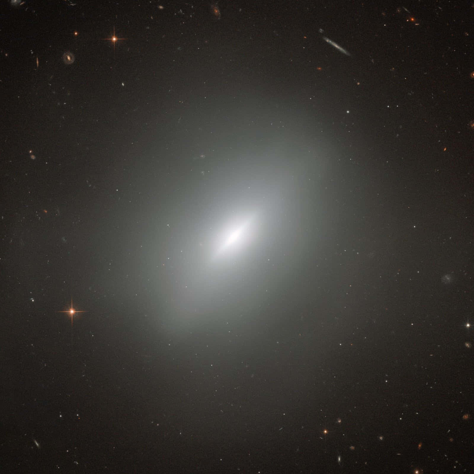 Elliptical Galaxy 桌布 壁紙 — 一個明亮的螺旋星系在點綴著遙遠星系和閃爍星星的星場中柔和地發光。