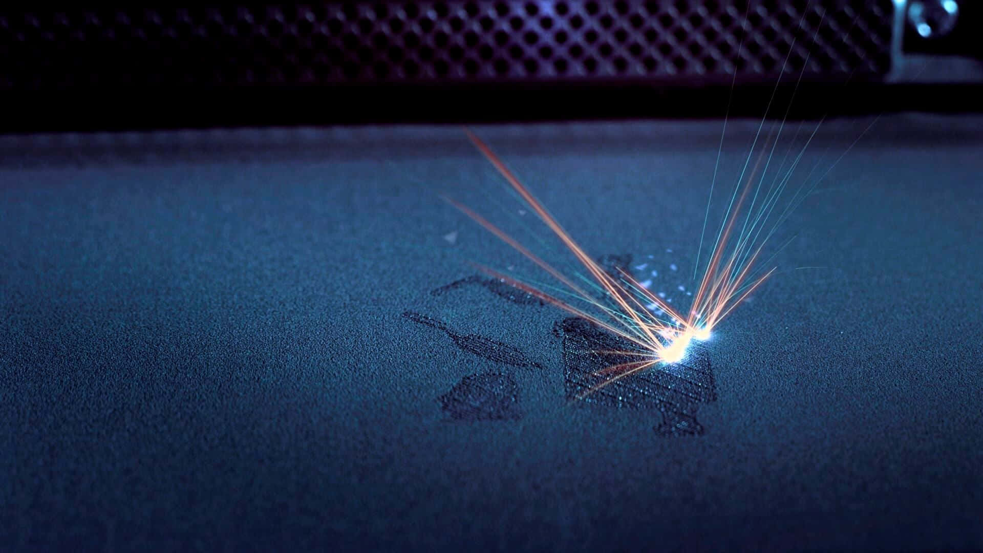 3d Printer 桌布 壁紙 — 一個明亮的雷射點在昏暗燈光下，於深色紋理表面激起鮮豔的橙色和藍色軌跡。
