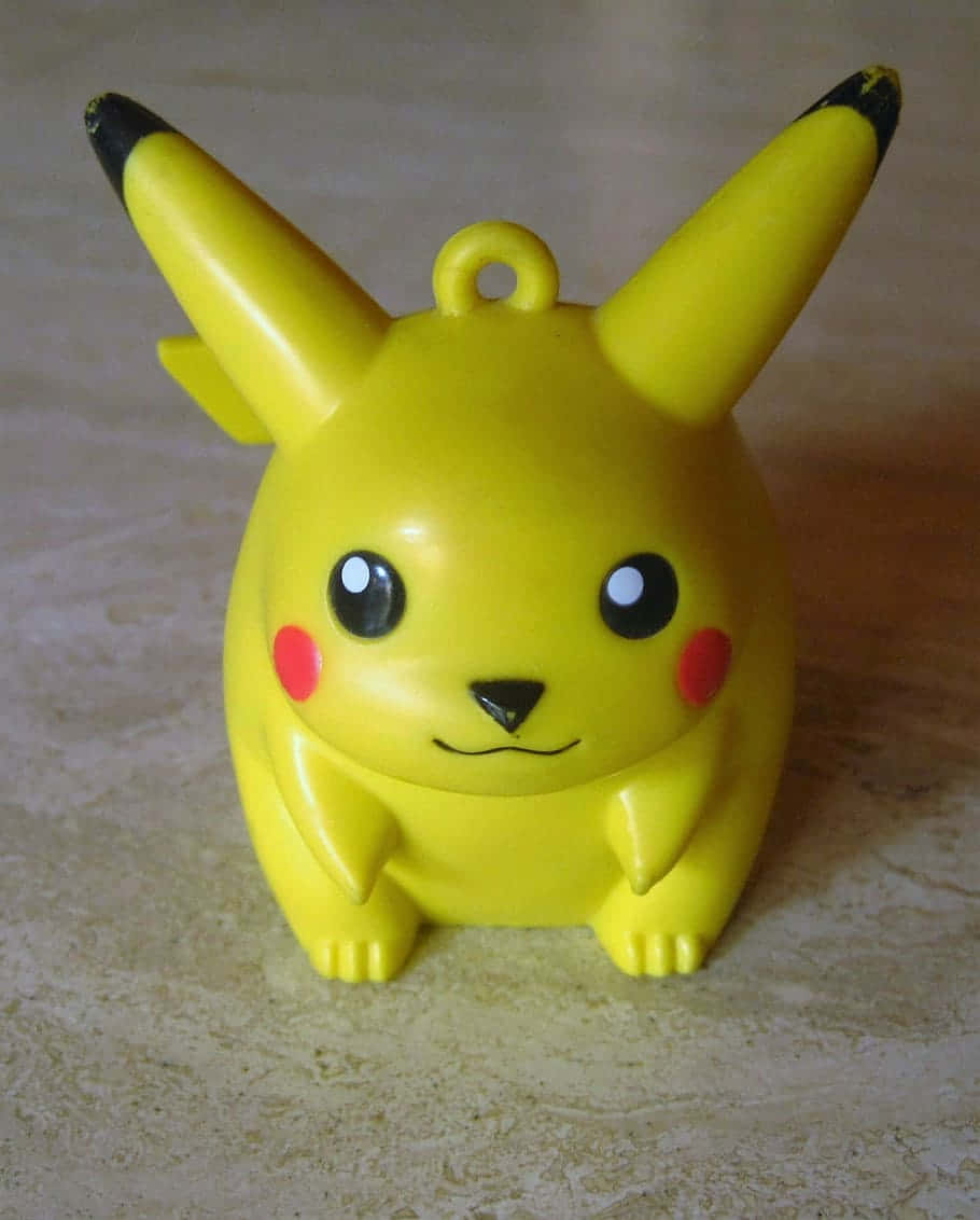 Pokemon Toys 桌布 壁紙 — 一個明亮的黃色皮卡丘公仔，有紅色臉頰和黑色尖端耳朵，坐在米色瓷磚表面上。