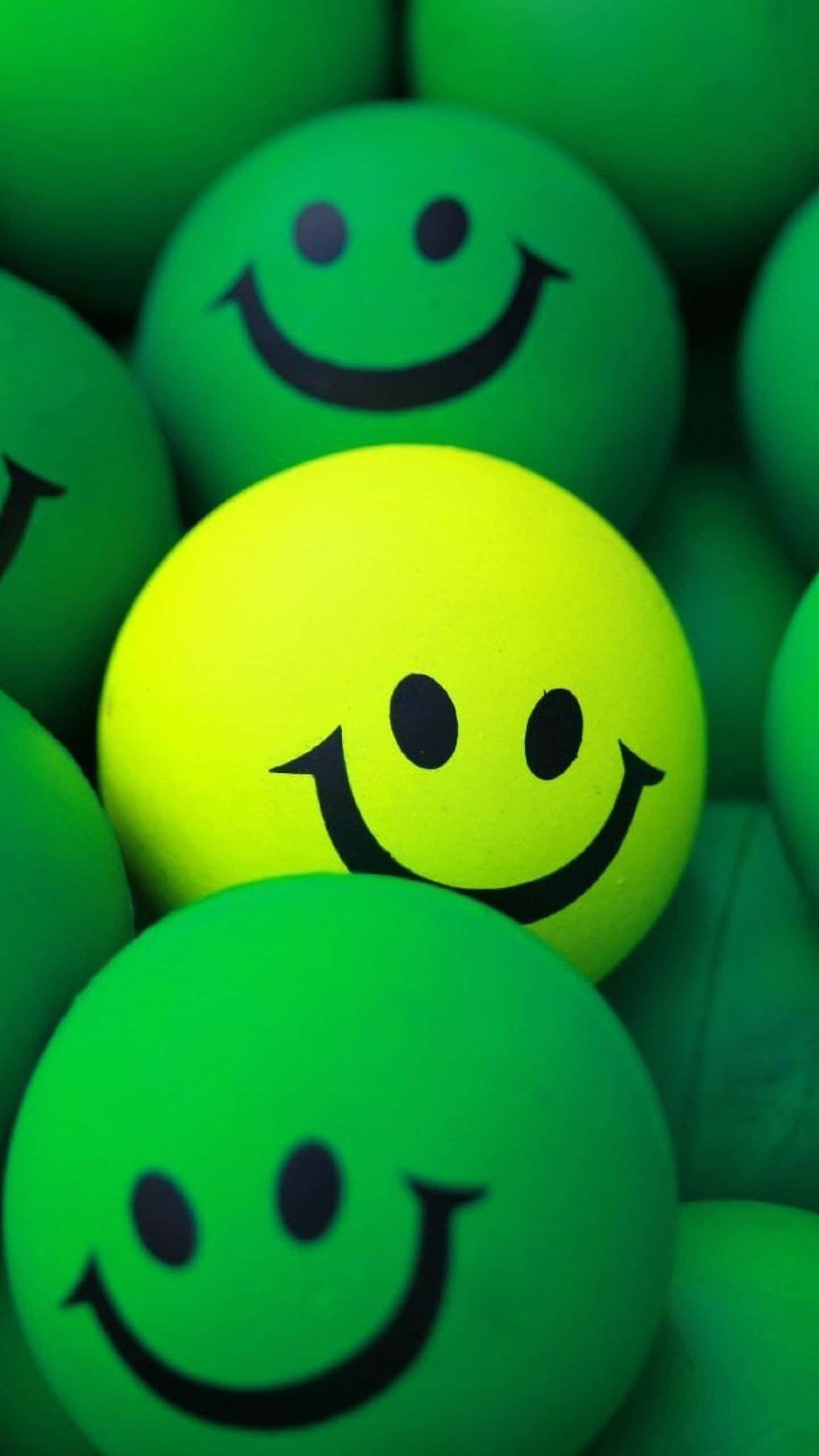 Smile 桌布 壁紙 — 一個明亮的黃色笑臉球，被綠色笑臉球包圍的特寫鏡頭。